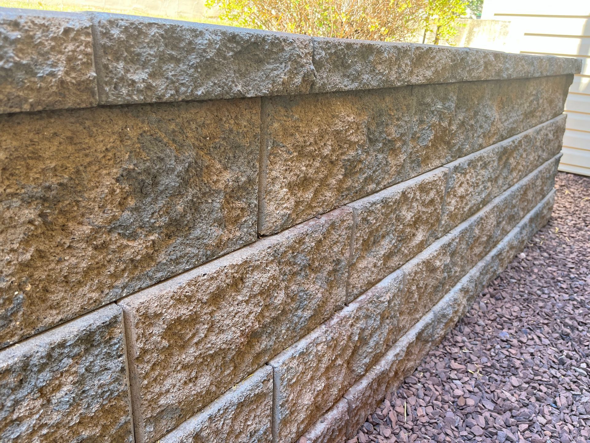 Stone retaining wall with horizontal tiers beside a gravel path in daylight