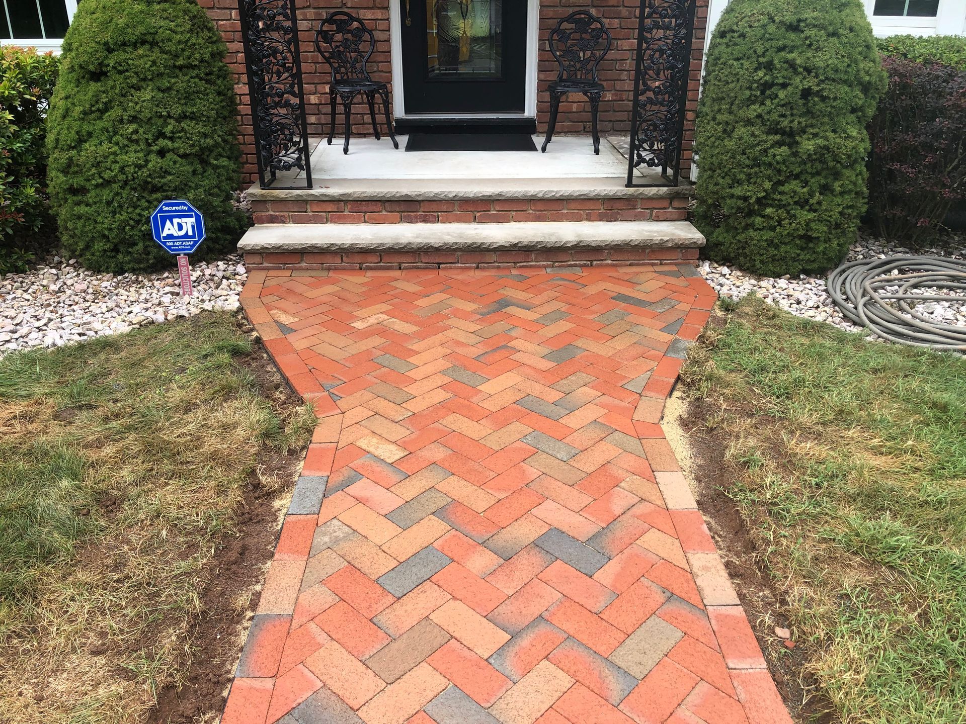 Brick walkway leading to a front porch between trimmed hedges and grass