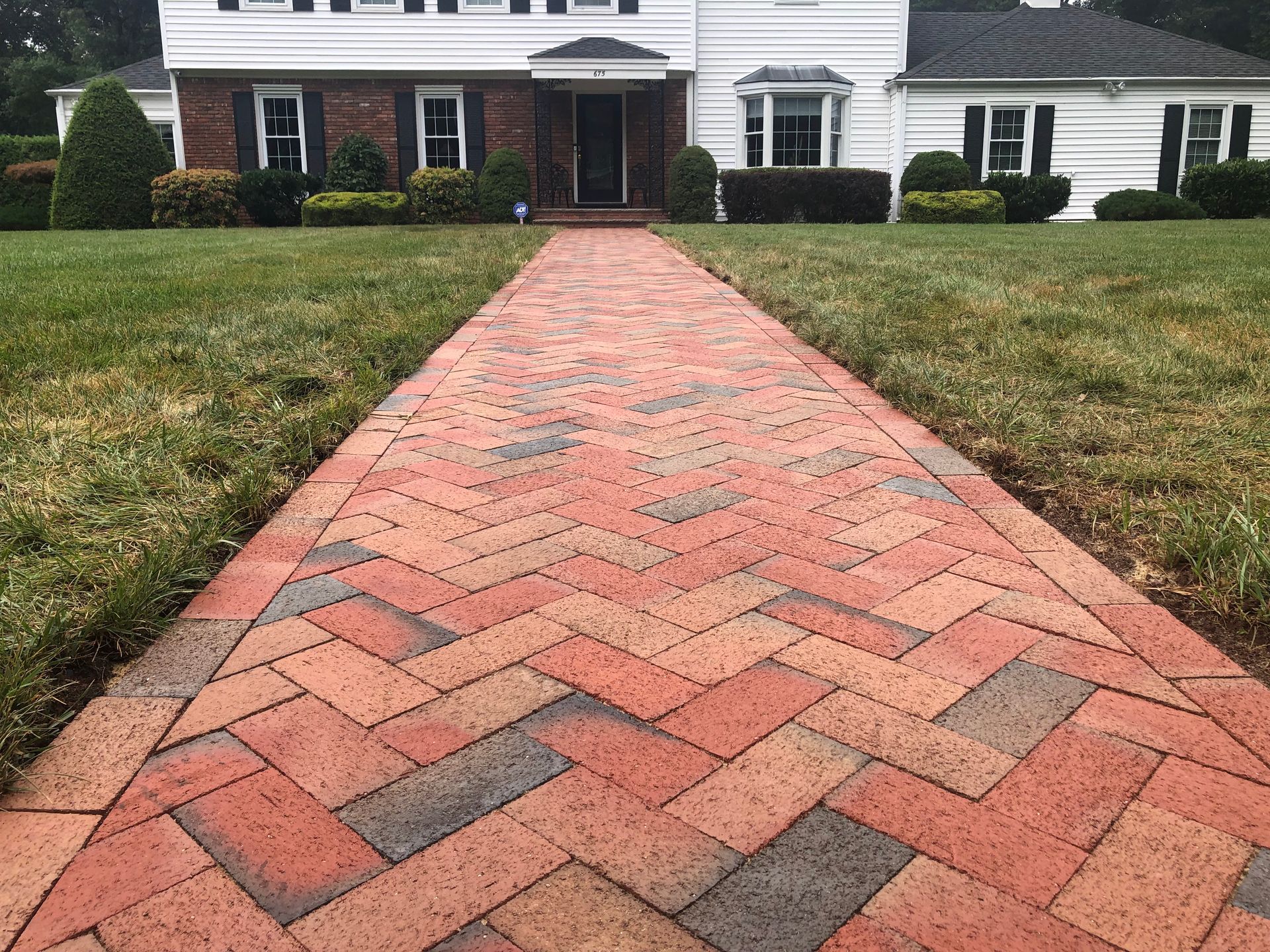 Brick walkway leading to a white house with dark shutters and a front door