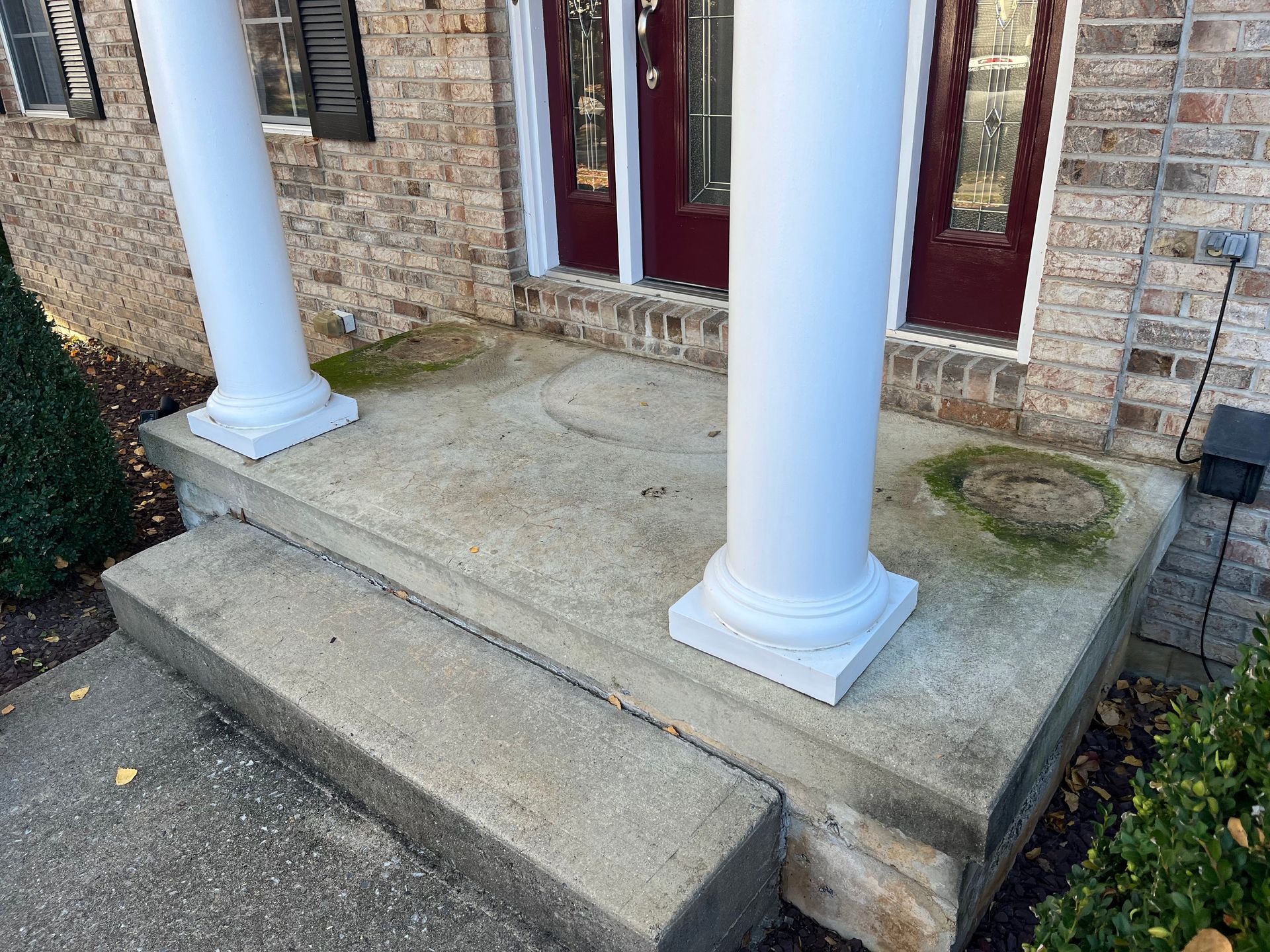 Front porch with two white columns and a short set of concrete steps leading to red doors.