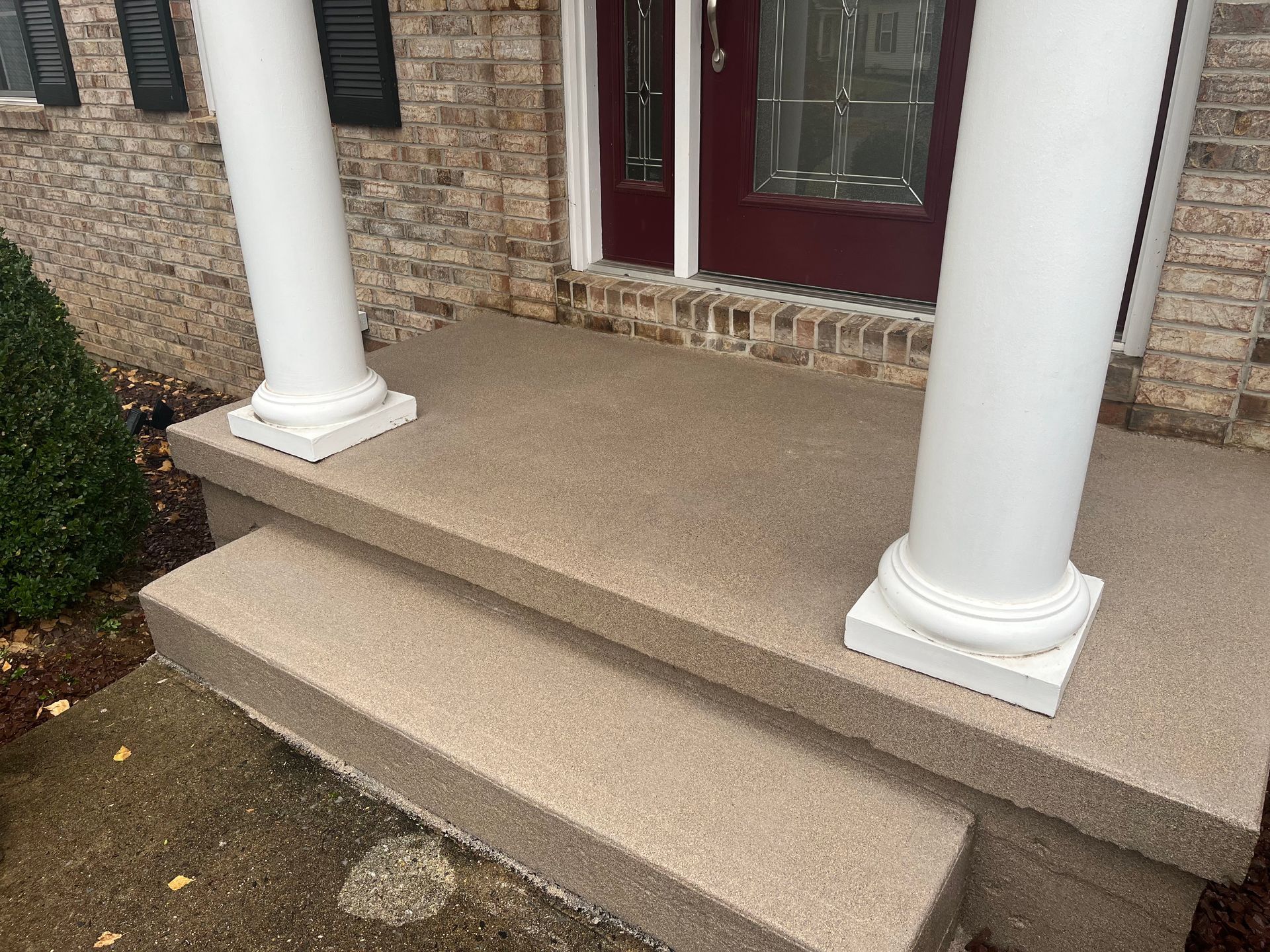 Front porch with tan steps, white columns, and a red front door on a brick house.