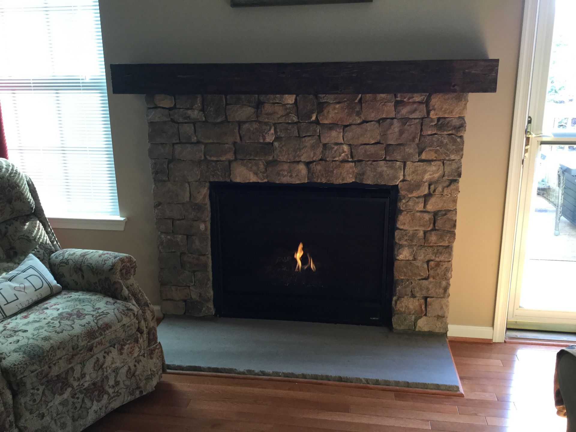 Living room fireplace with stone surround, dark mantle, and a small fire burning