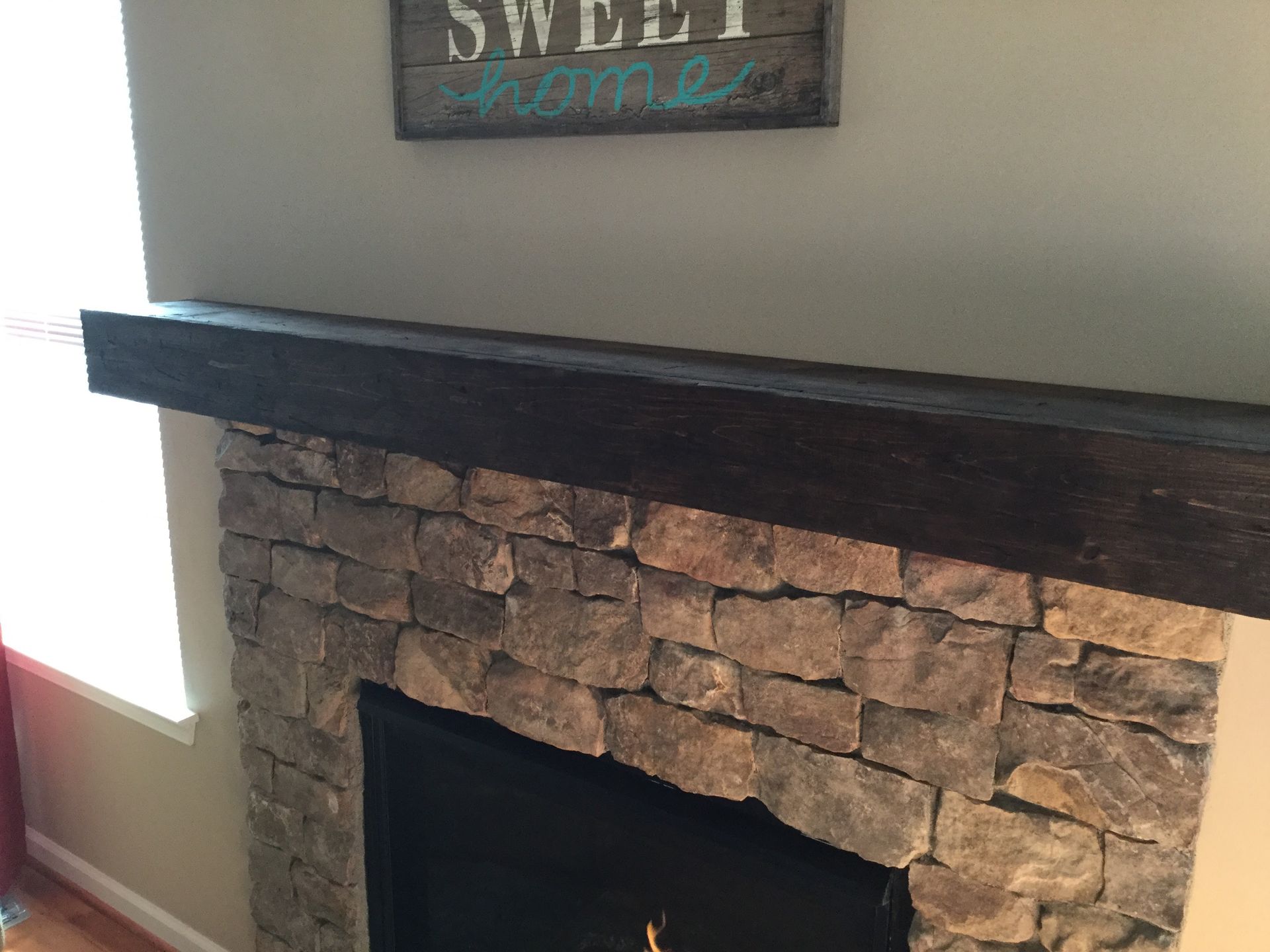 Stone fireplace with dark wood mantel and a “Sweet Home” sign above it