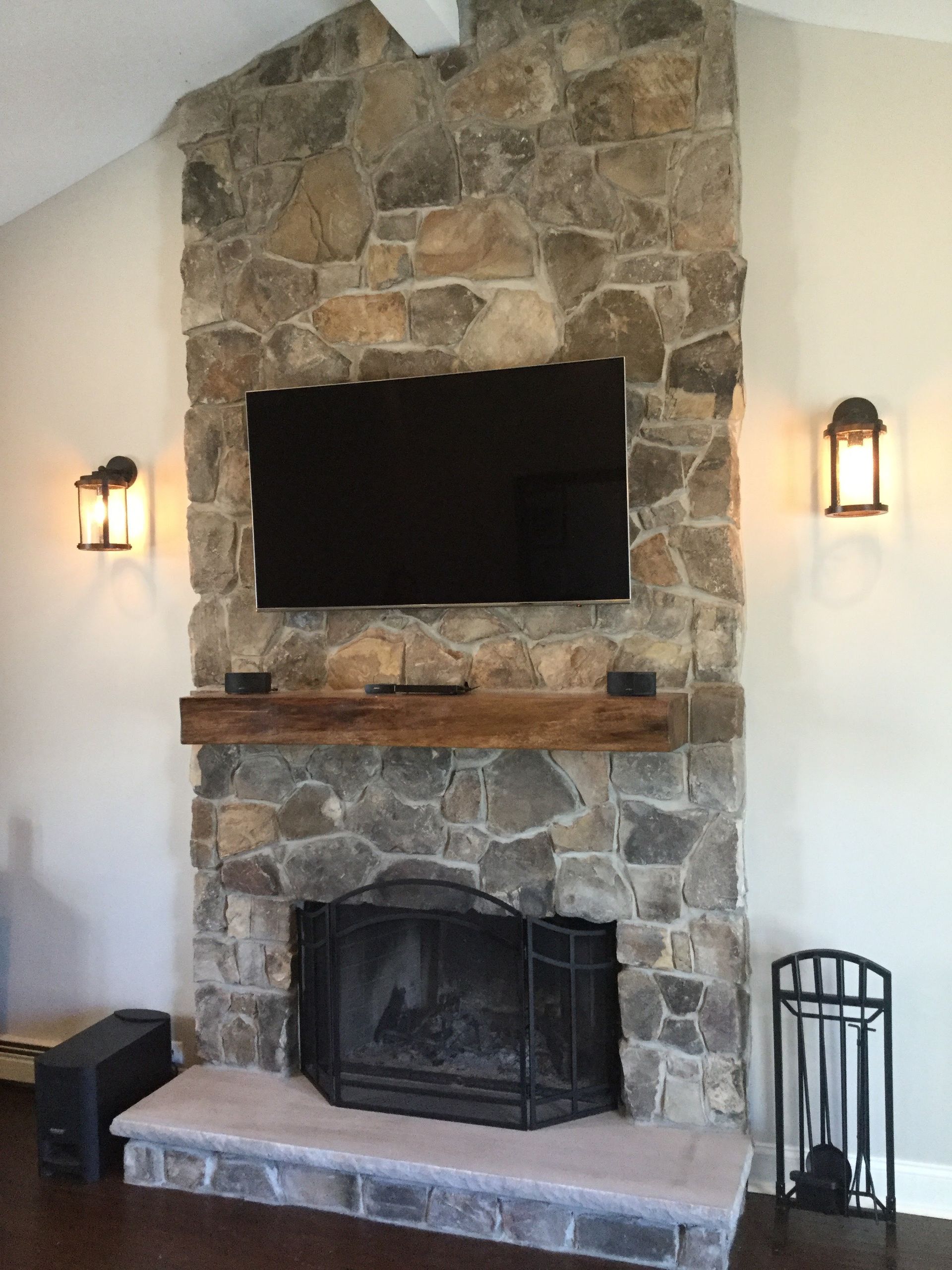 Stone fireplace with mounted TV, lit wall sconces, and a black screen insert in a living room