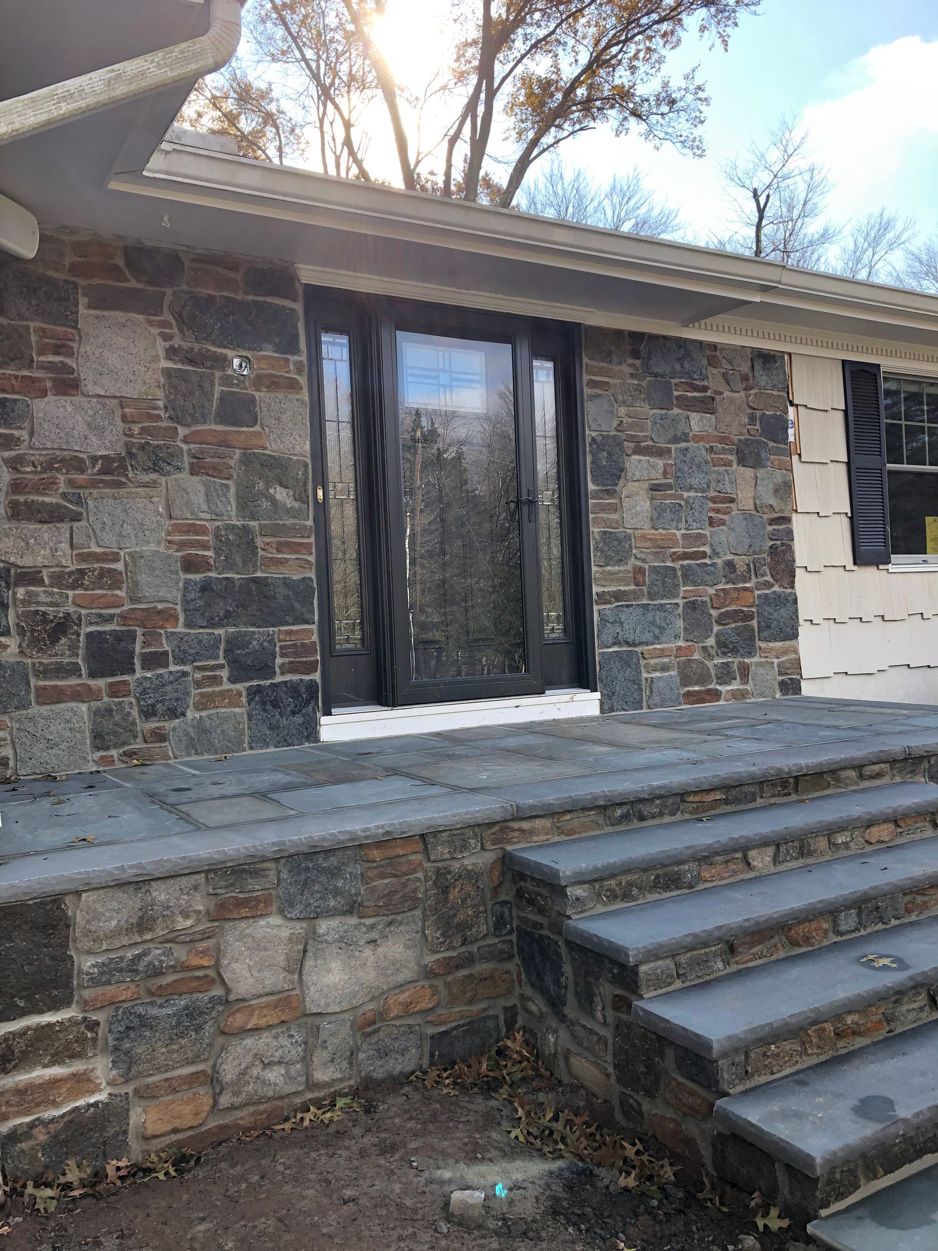 Stone house exterior with steps leading to a dark glass double door and a stone porch wall