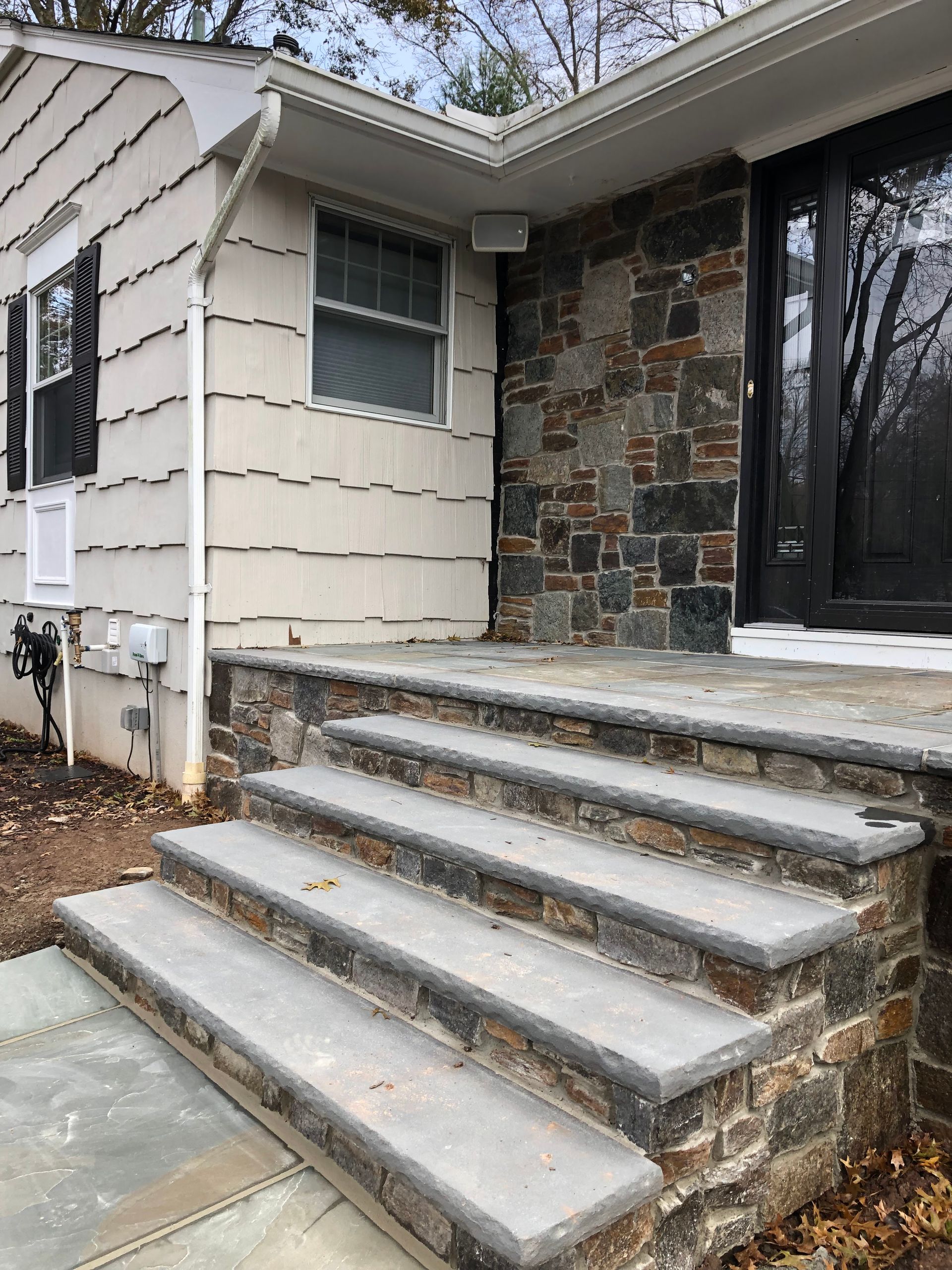 Concrete front steps leading to a house entry with stone and beige siding, lightly dusted with snow.