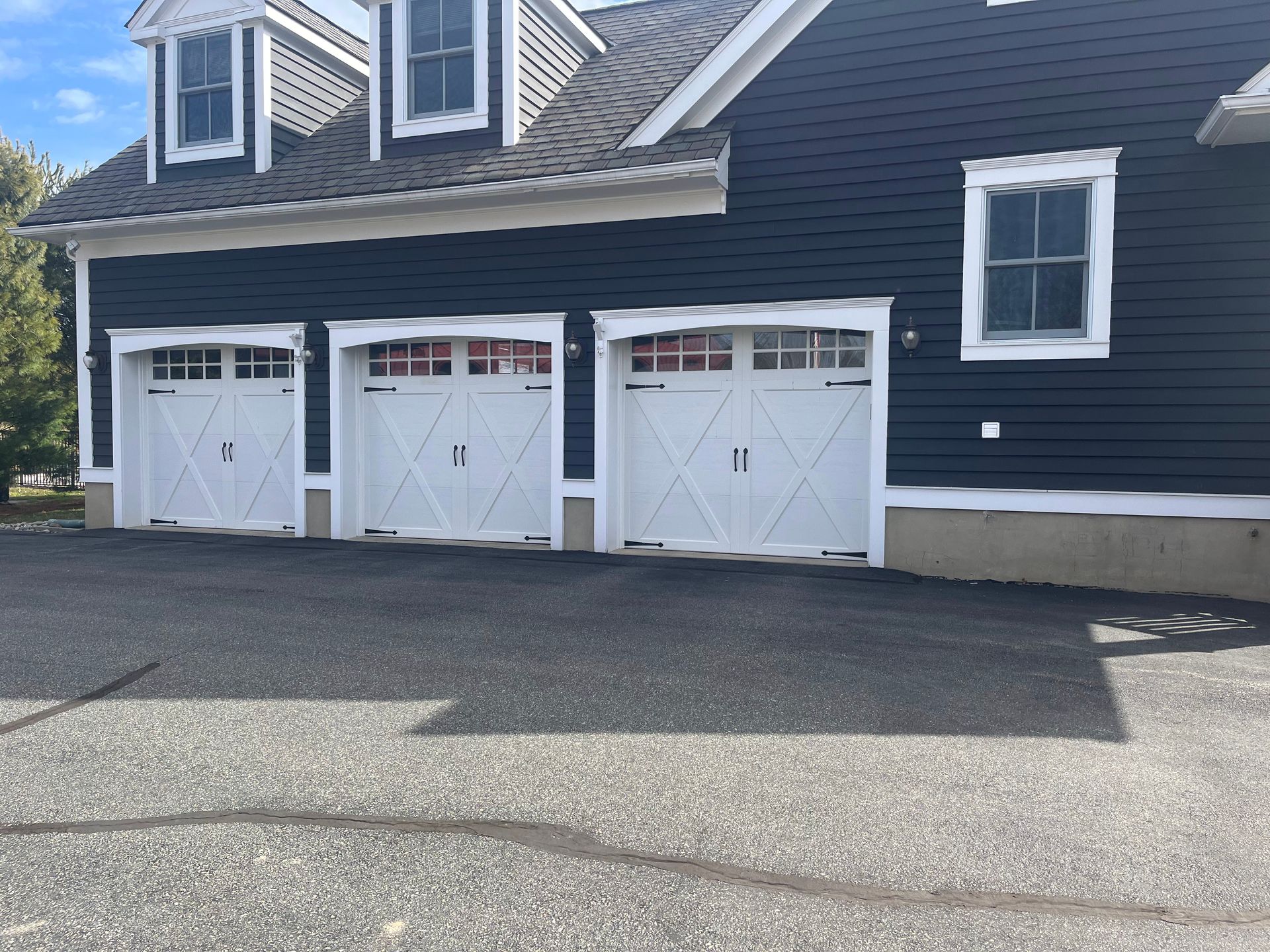 Three white garage doors on a dark blue house with a paved driveway.