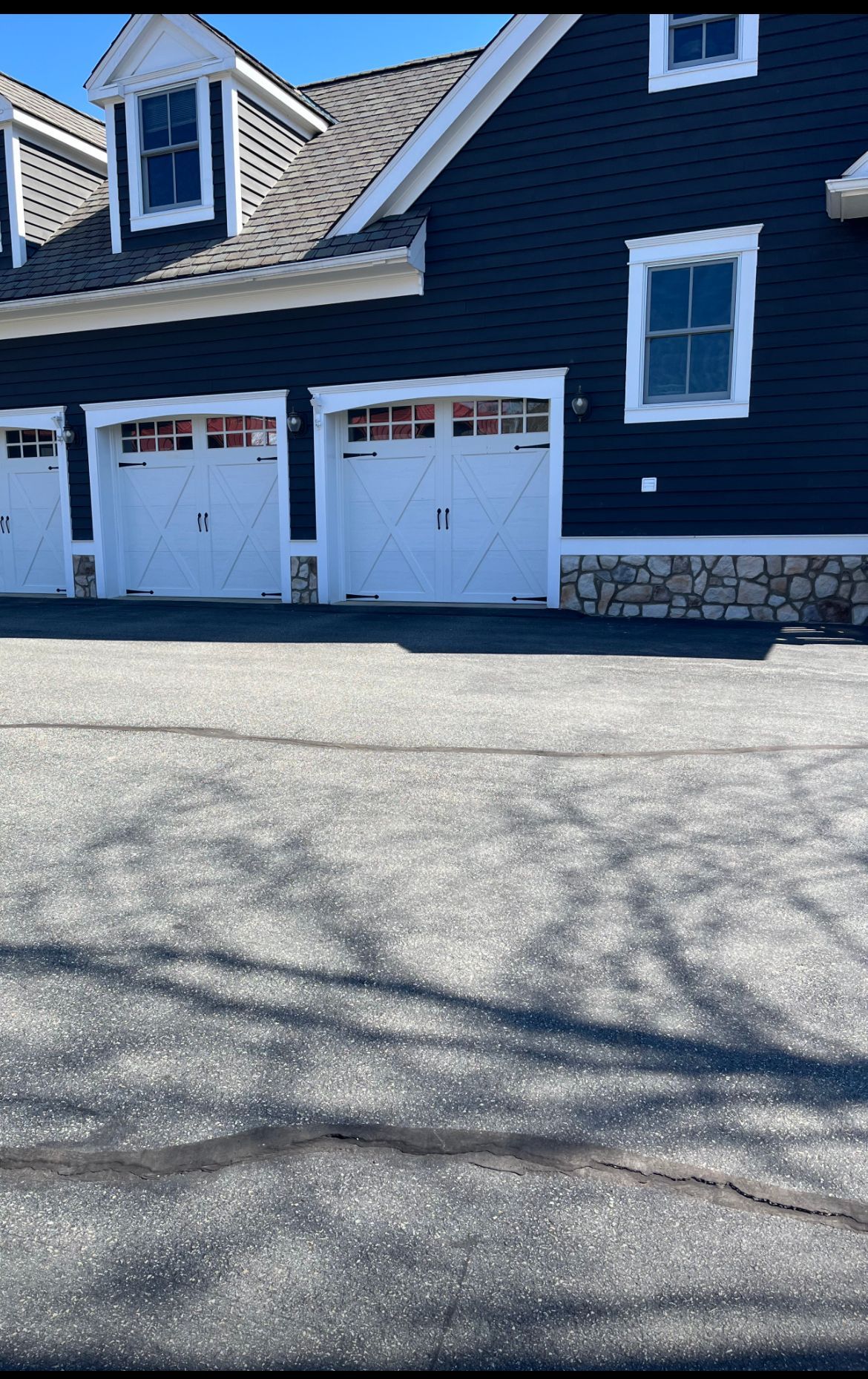 Blue house with two white garage doors and a paved driveway in front