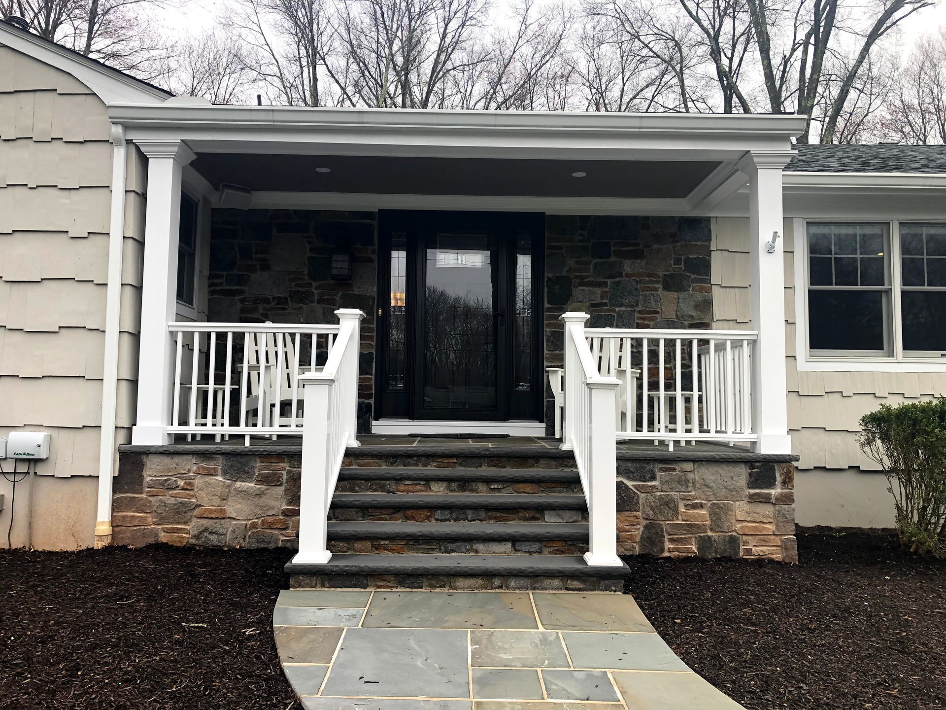 Front porch with stone steps, white railings, and a black glass door on a house exterior