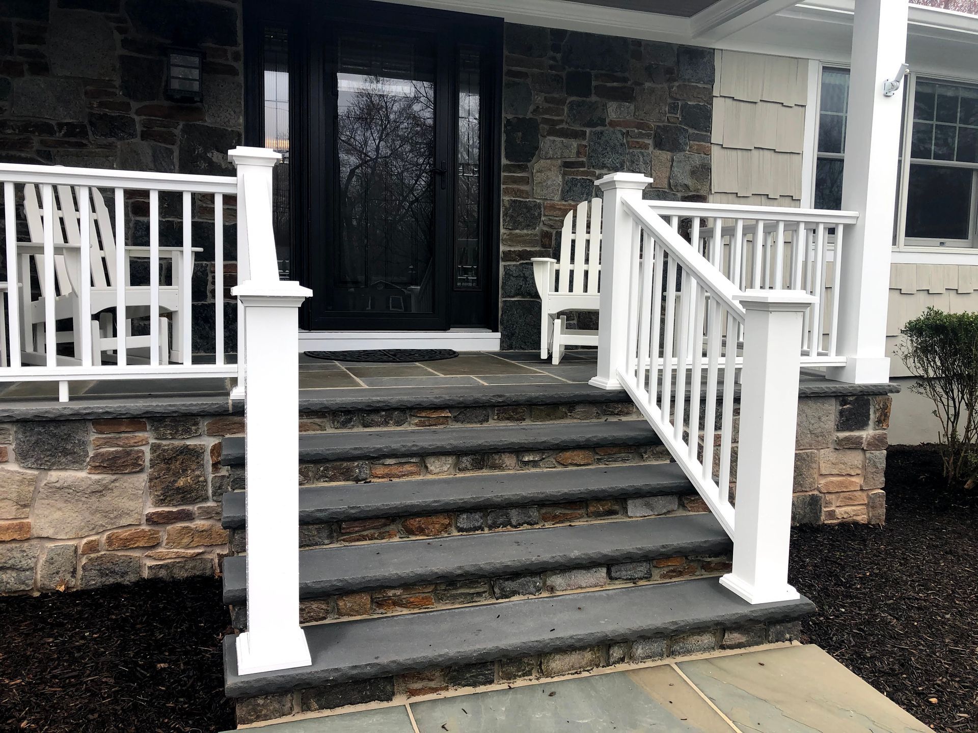 Front steps with white railings leading to a dark front door on a stone house.