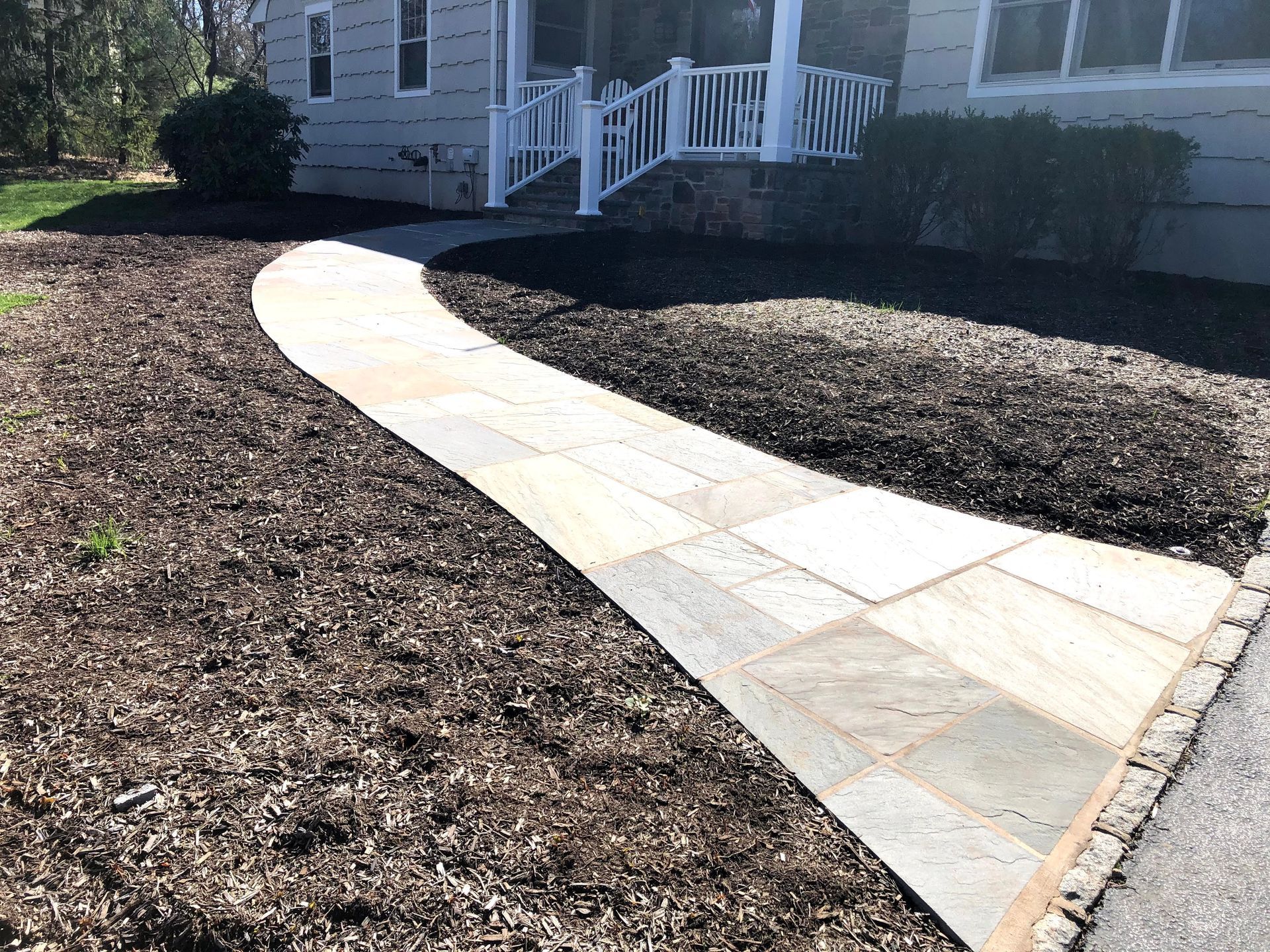 Curved white stone walkway leading to a house porch through a mulched yard
