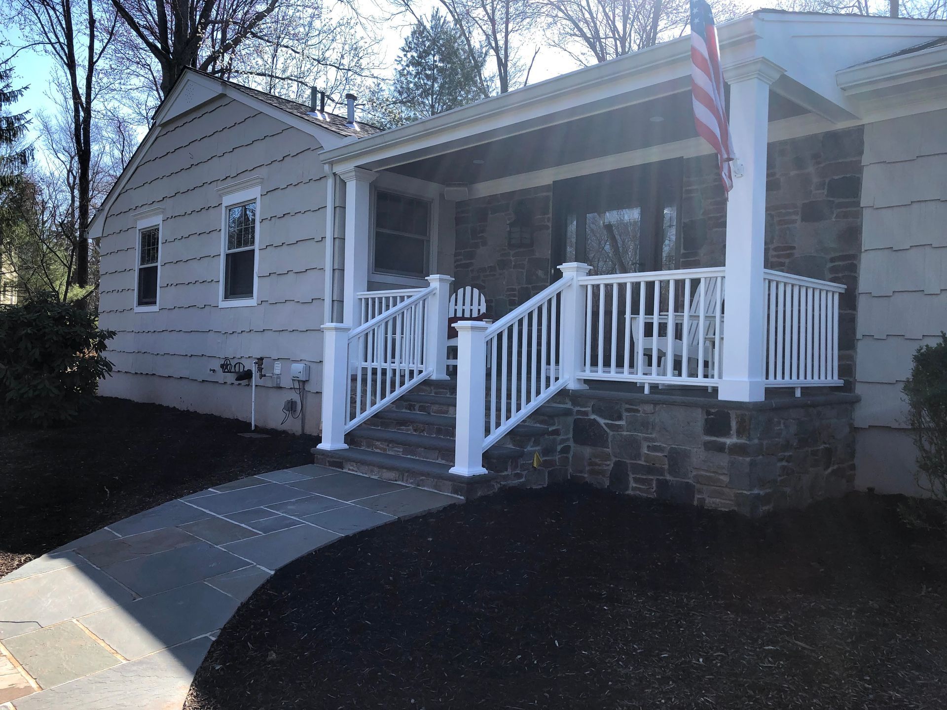 Single-story house with white porch railings, stone steps, and an American flag by the entrance