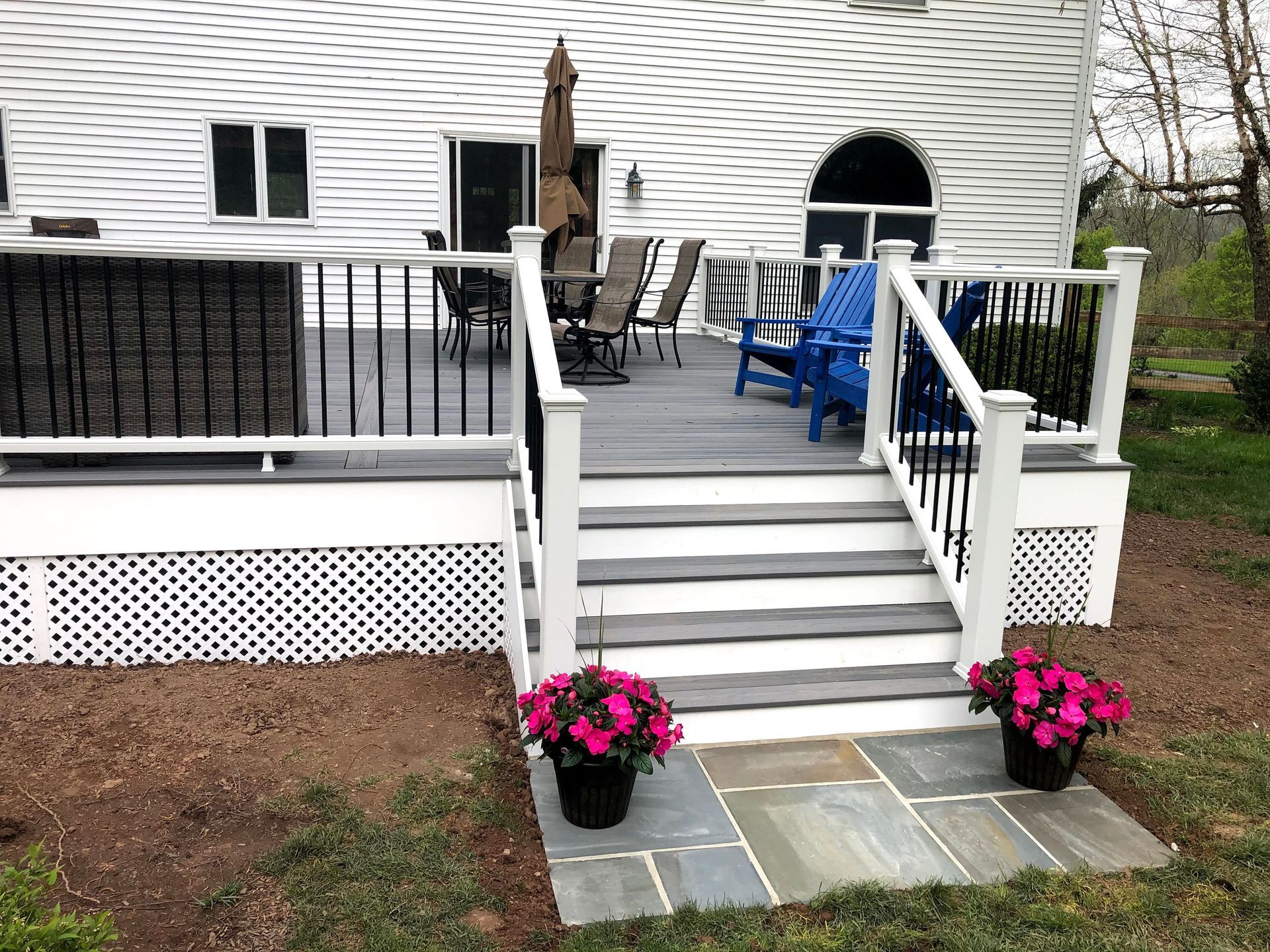 Front porch with white stairs, black railings, potted pink flowers, and blue outdoor chairs.