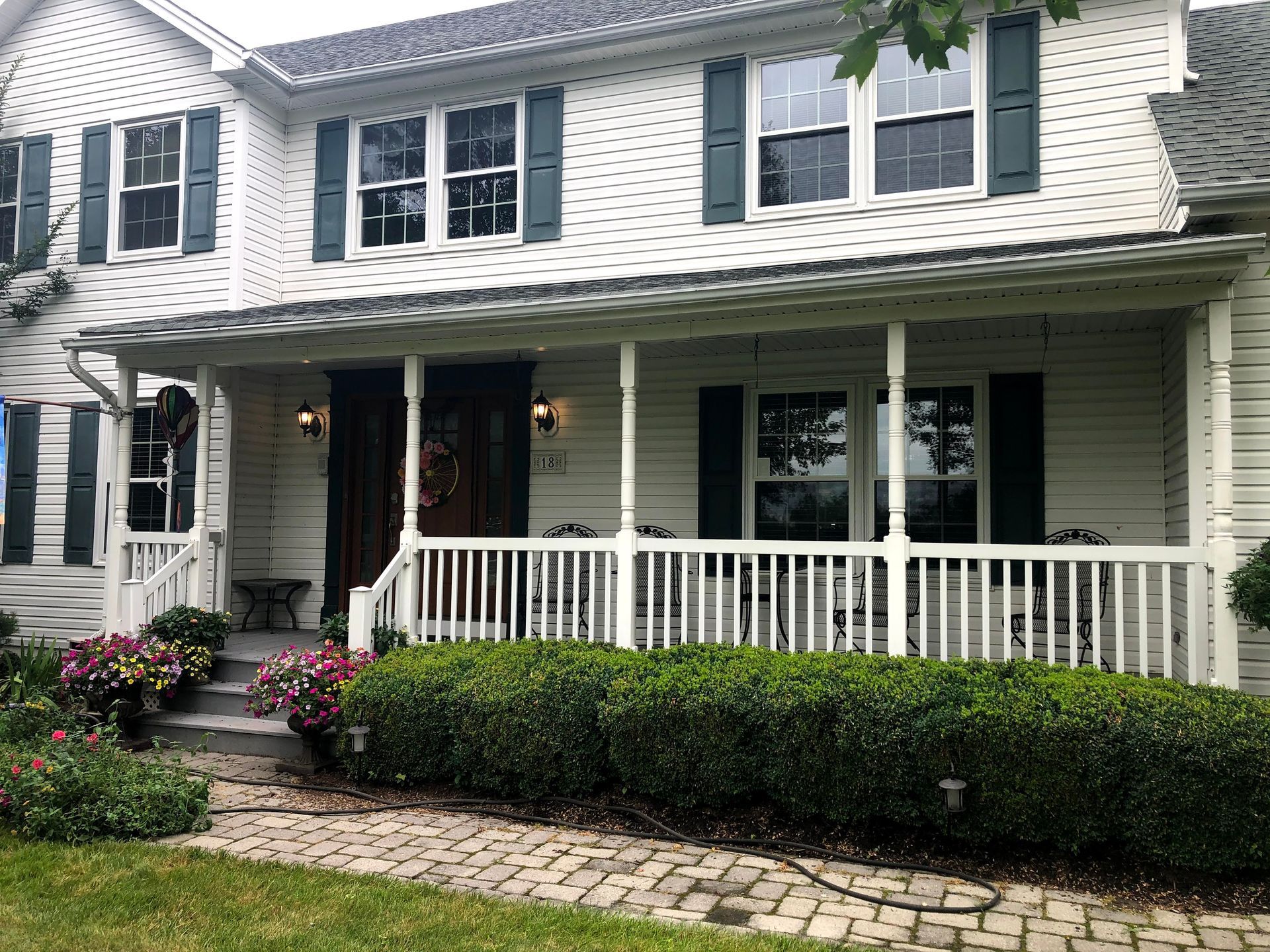 Two-story white house with black shutters, covered porch, and neatly trimmed shrubs in front