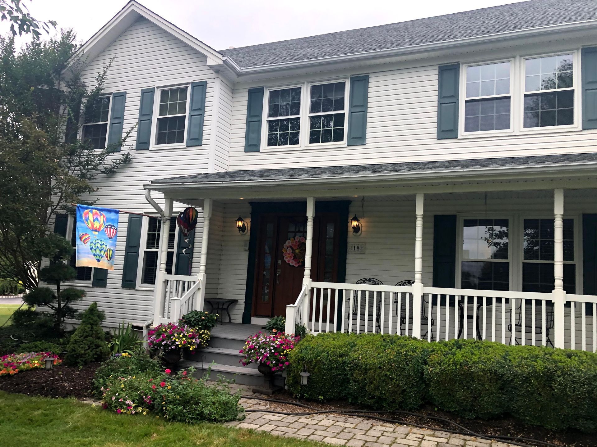 Two-story white house with black shutters, front porch, and flower beds in front yard