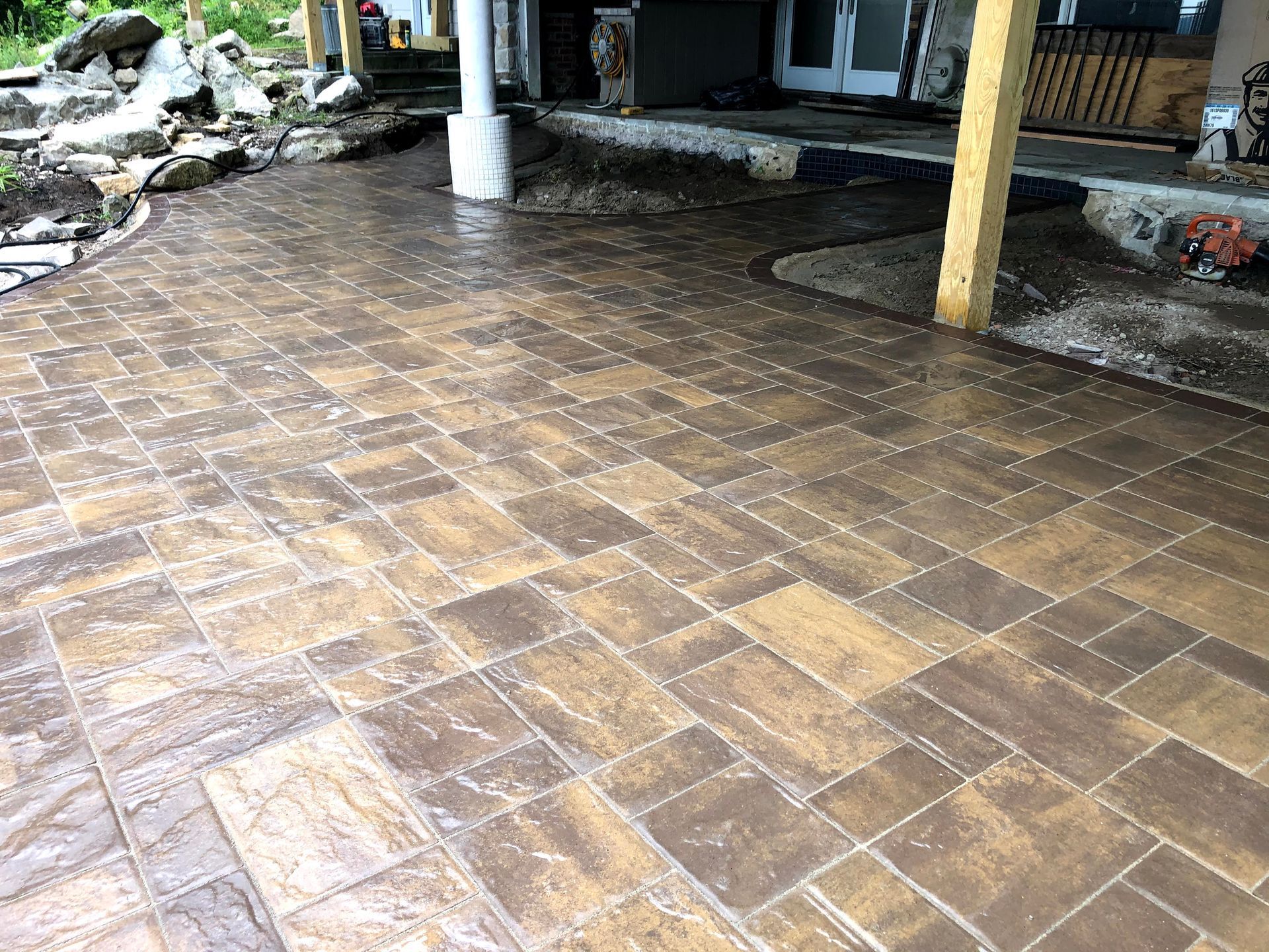 Wet brick patio under a covered outdoor area with a white post and wooden support beam