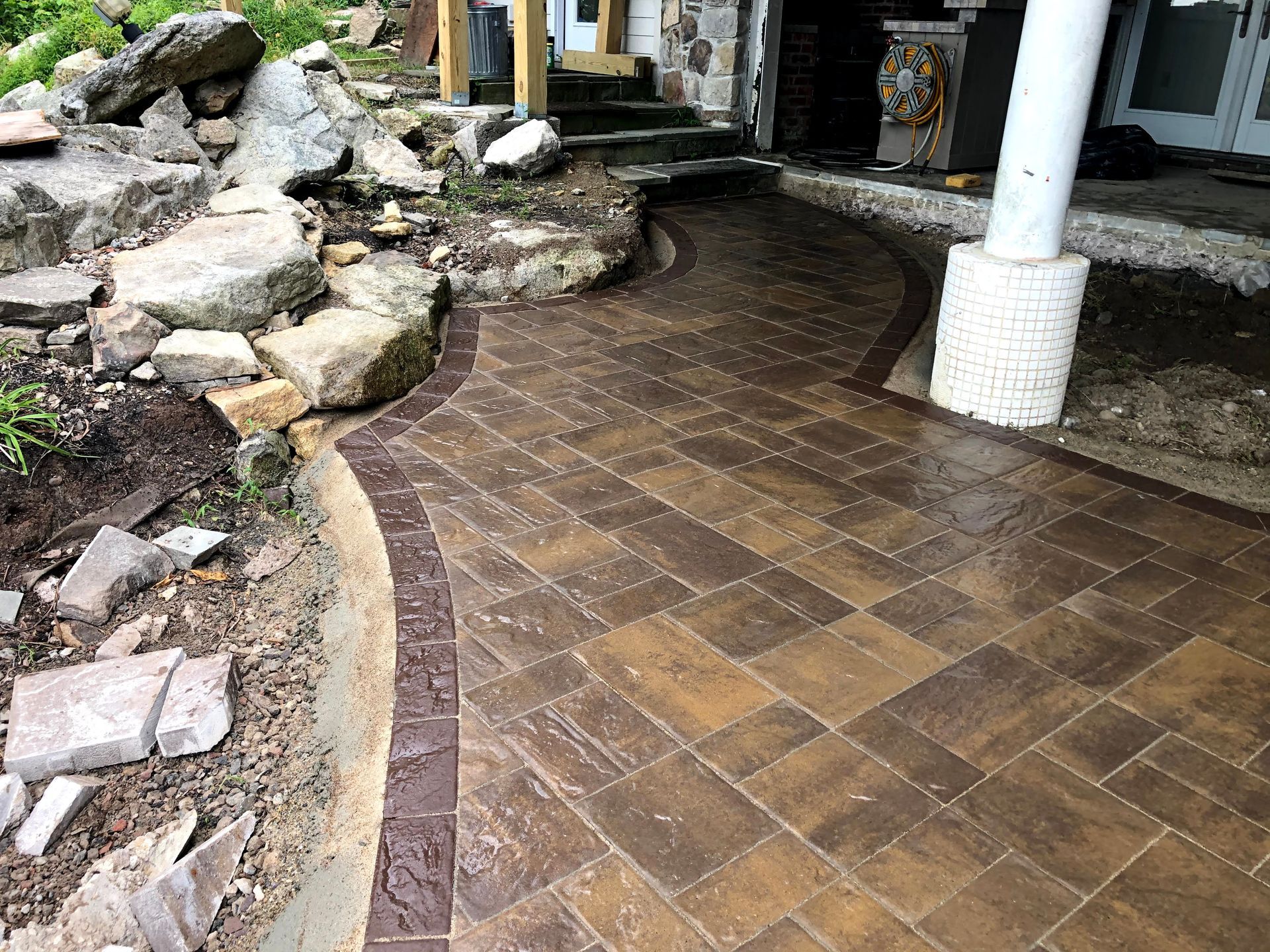 Curved brown brick walkway beside rocks and a white column in a garden-like area
