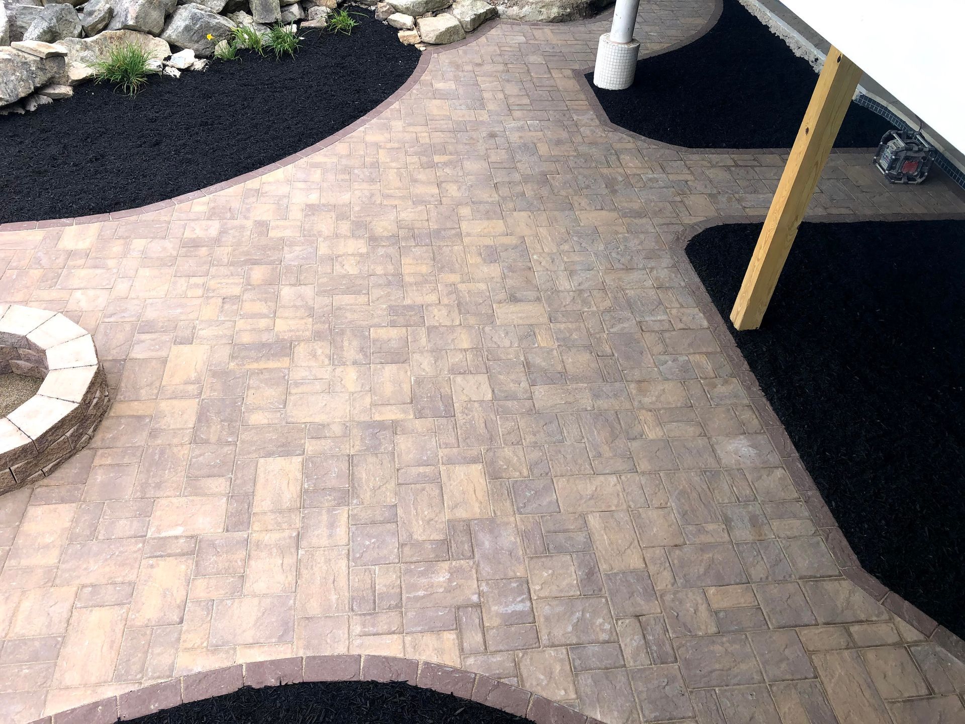 Curved tan brick walkway bordered by black mulch and landscaping stones near a porch column