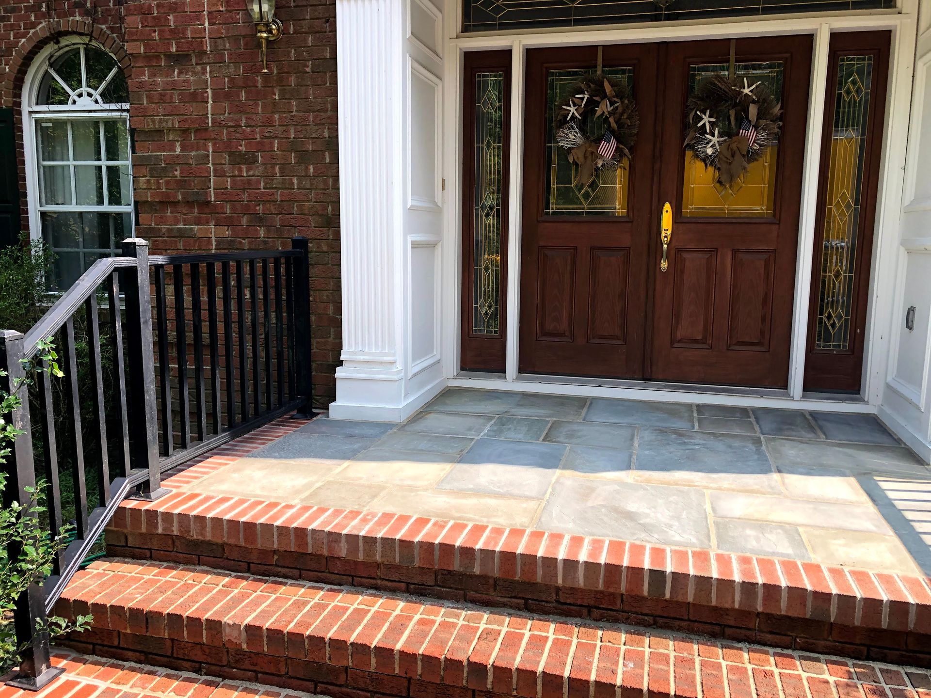 Brick porch with red steps, white columns, black railing, and wooden double doors