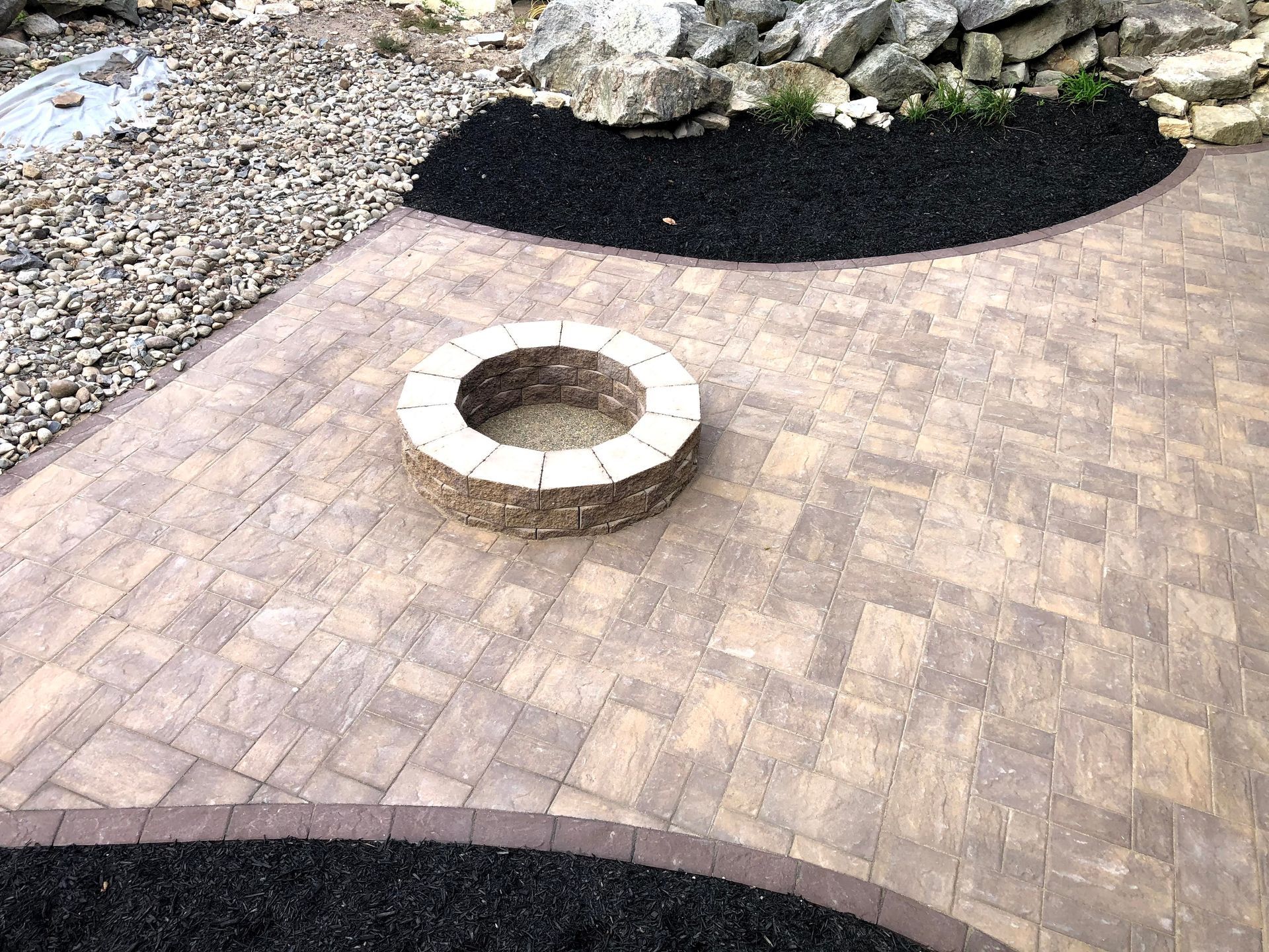 Brick patio with a circular fire pit beside a landscaped gravel and mulch border