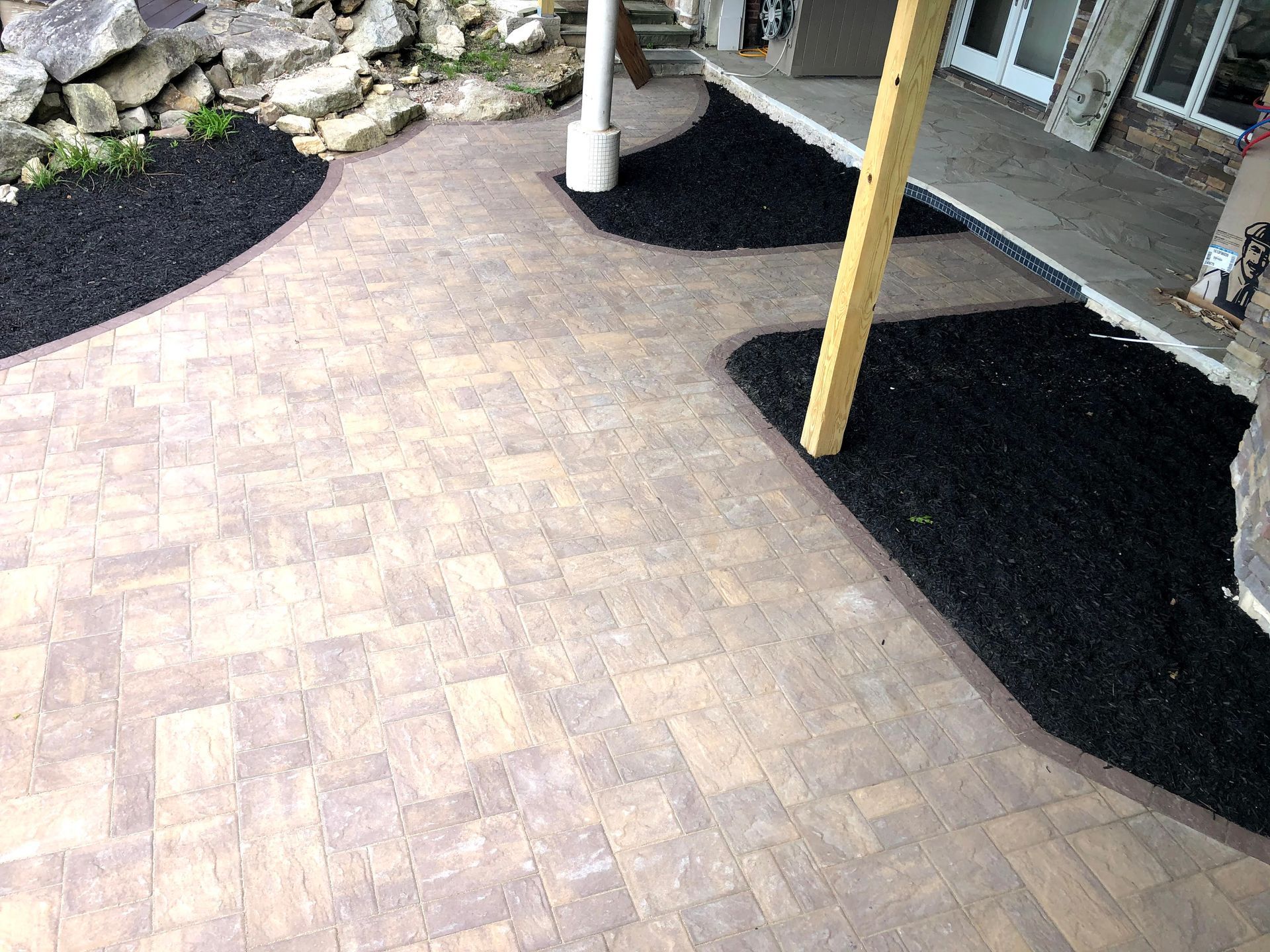Brick walkway beside house with black mulch beds and yellow support posts