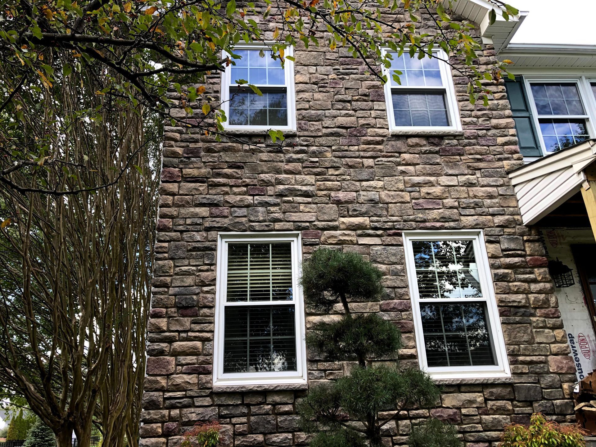 Stone house exterior with white-trimmed windows and a tree in front