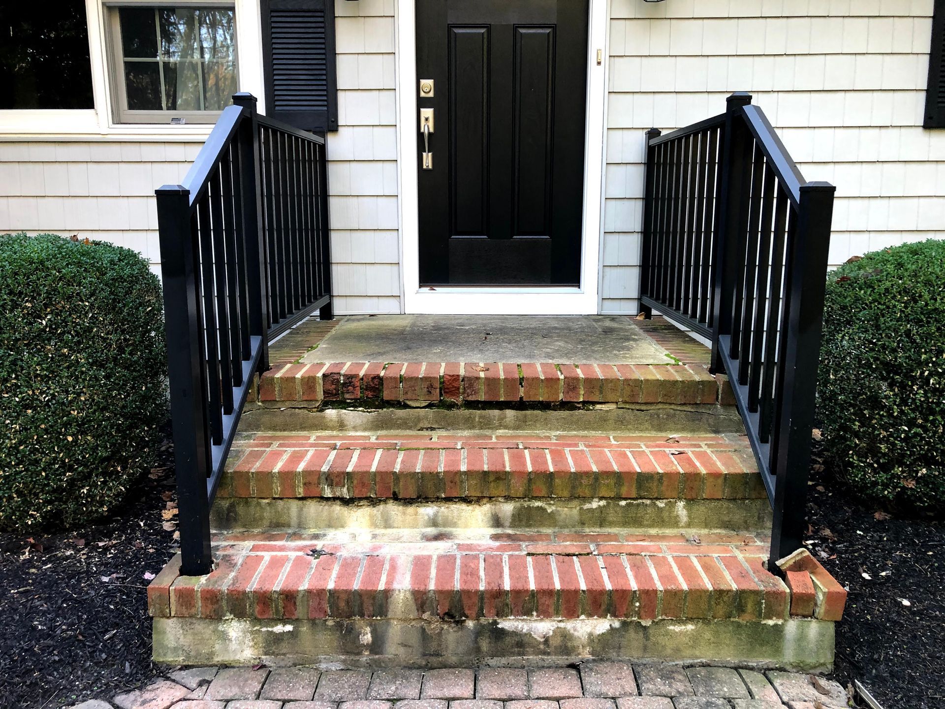 Front steps with brick risers and black railings leading to a black front door.