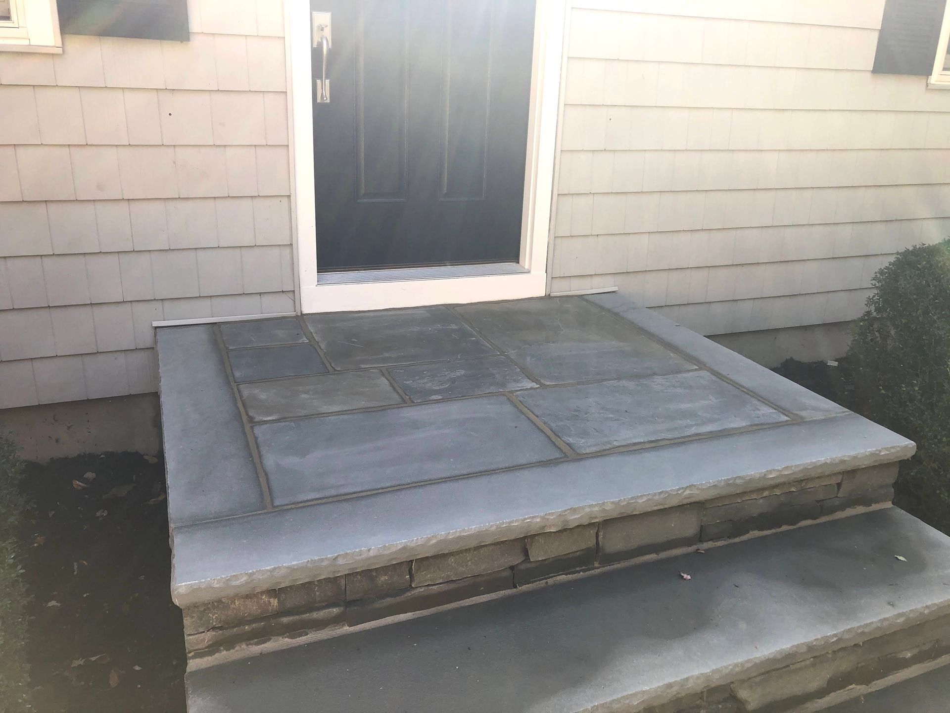 Concrete front steps and small porch with a door on a house exterior