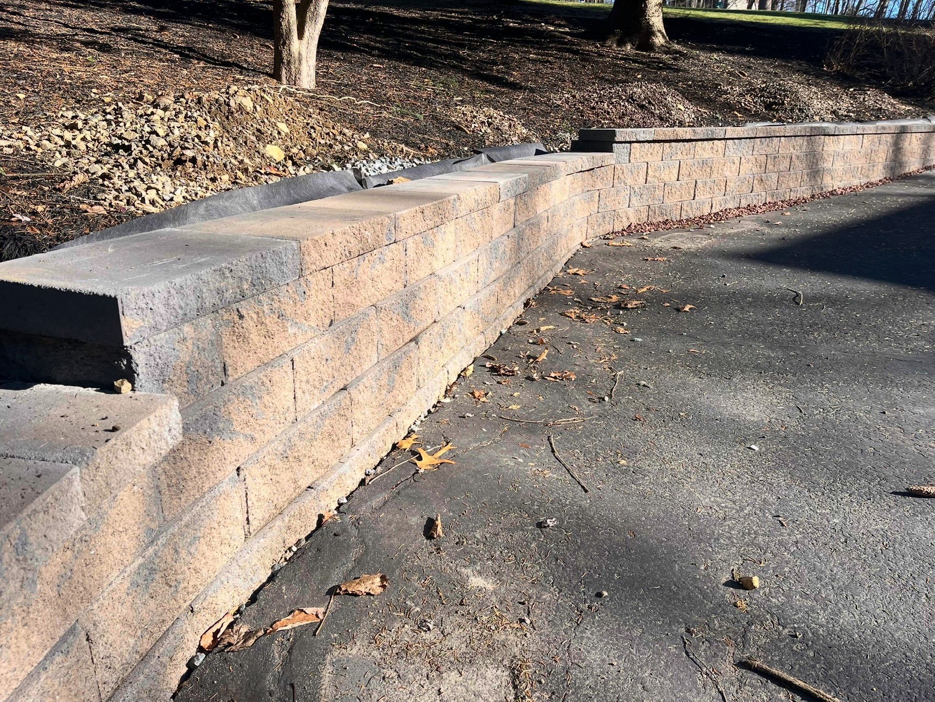 Low brick retaining wall along a paved path beside a tree-lined slope