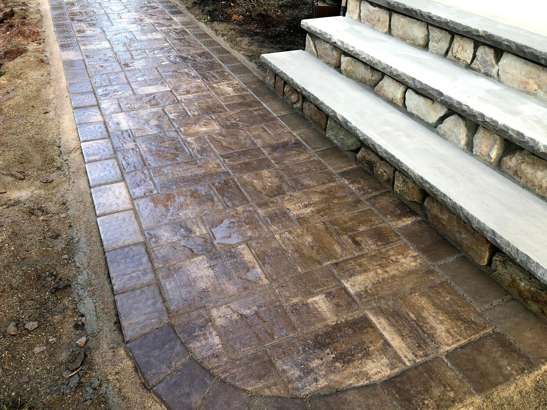 Brick walkway beside concrete steps, with a curved path and wet pavement.