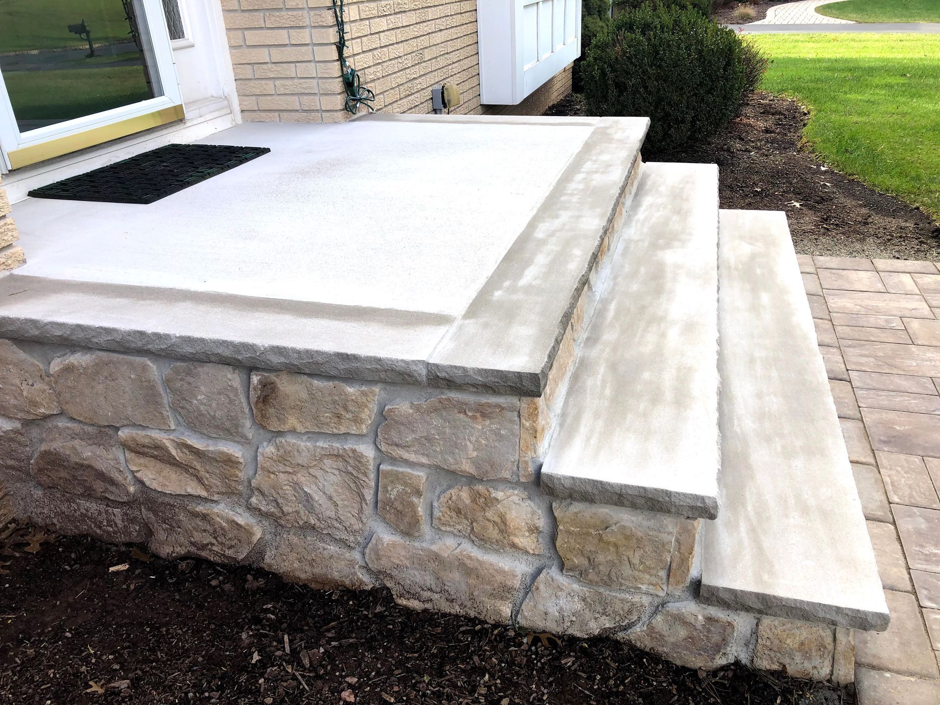 Stone front steps and porch with white concrete landing beside a house entrance