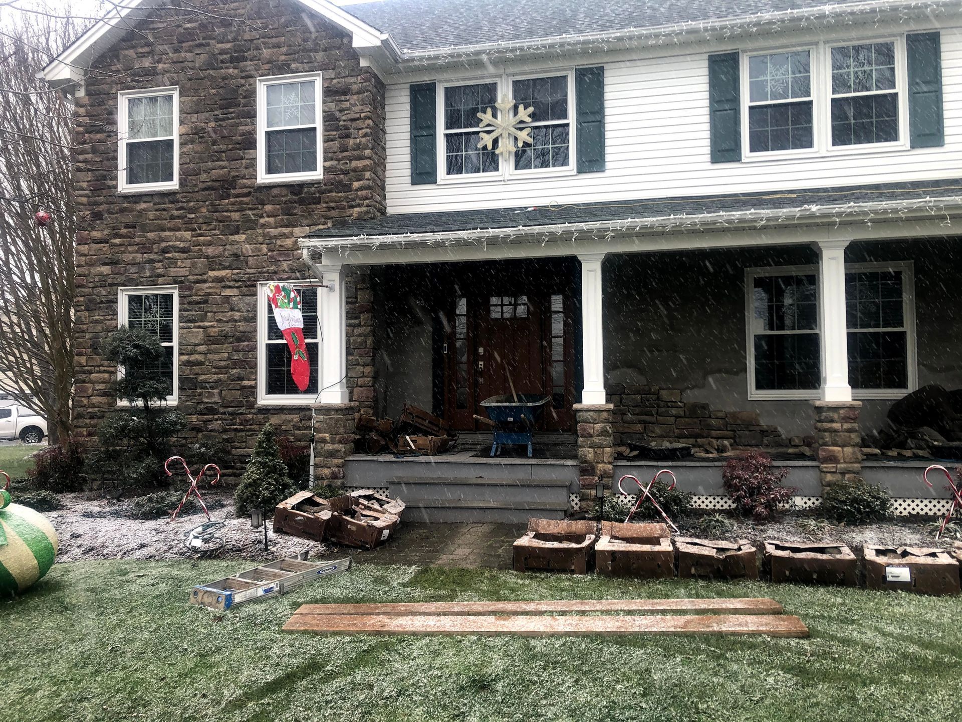 Two-story house with a front porch, stone facade, and snow-covered yard; a person stands in the doorway.