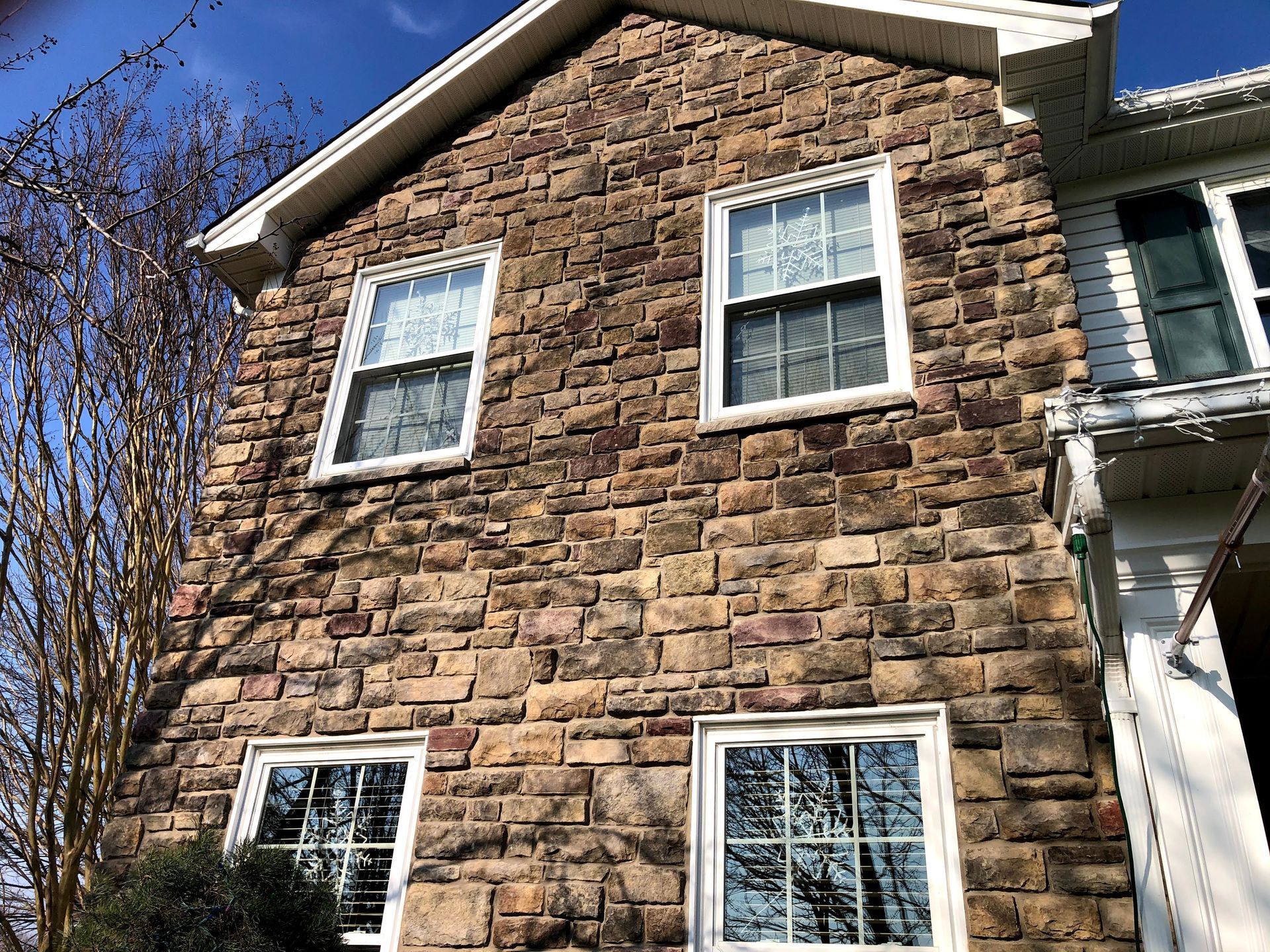 Stone house exterior with white-trimmed windows and a steep roof under a blue sky