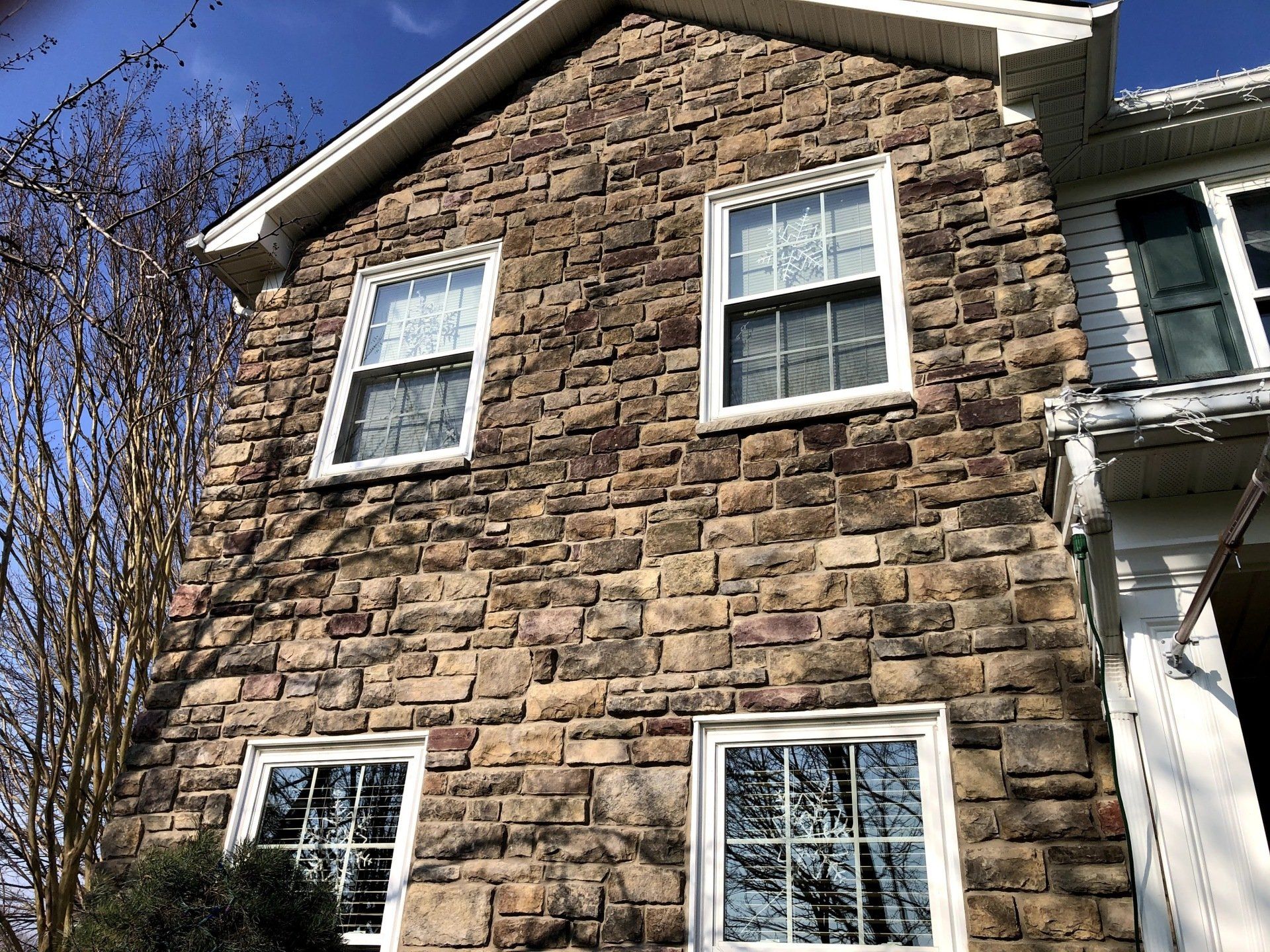 Stone house exterior with white-trimmed windows and a white gutter under a blue sky