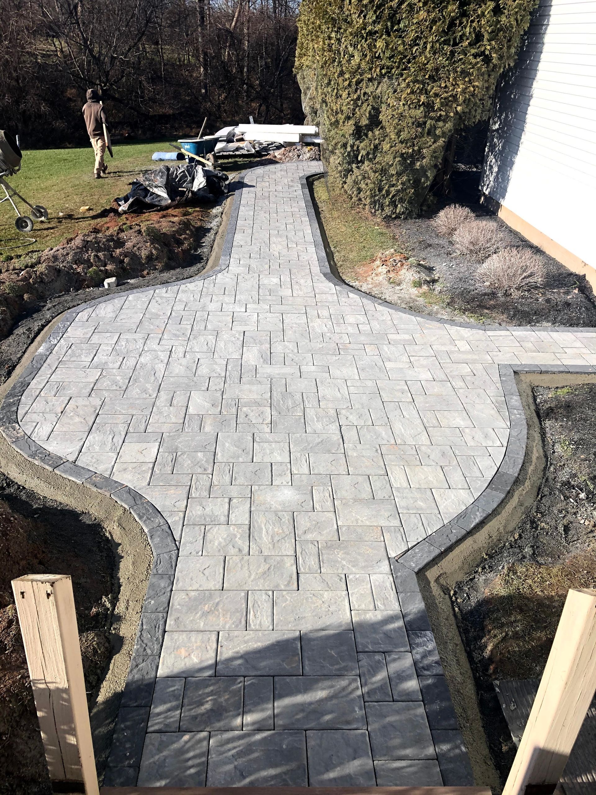 Curved gray paver walkway through a landscaped yard, bordered by dark mulch and low retaining edges.