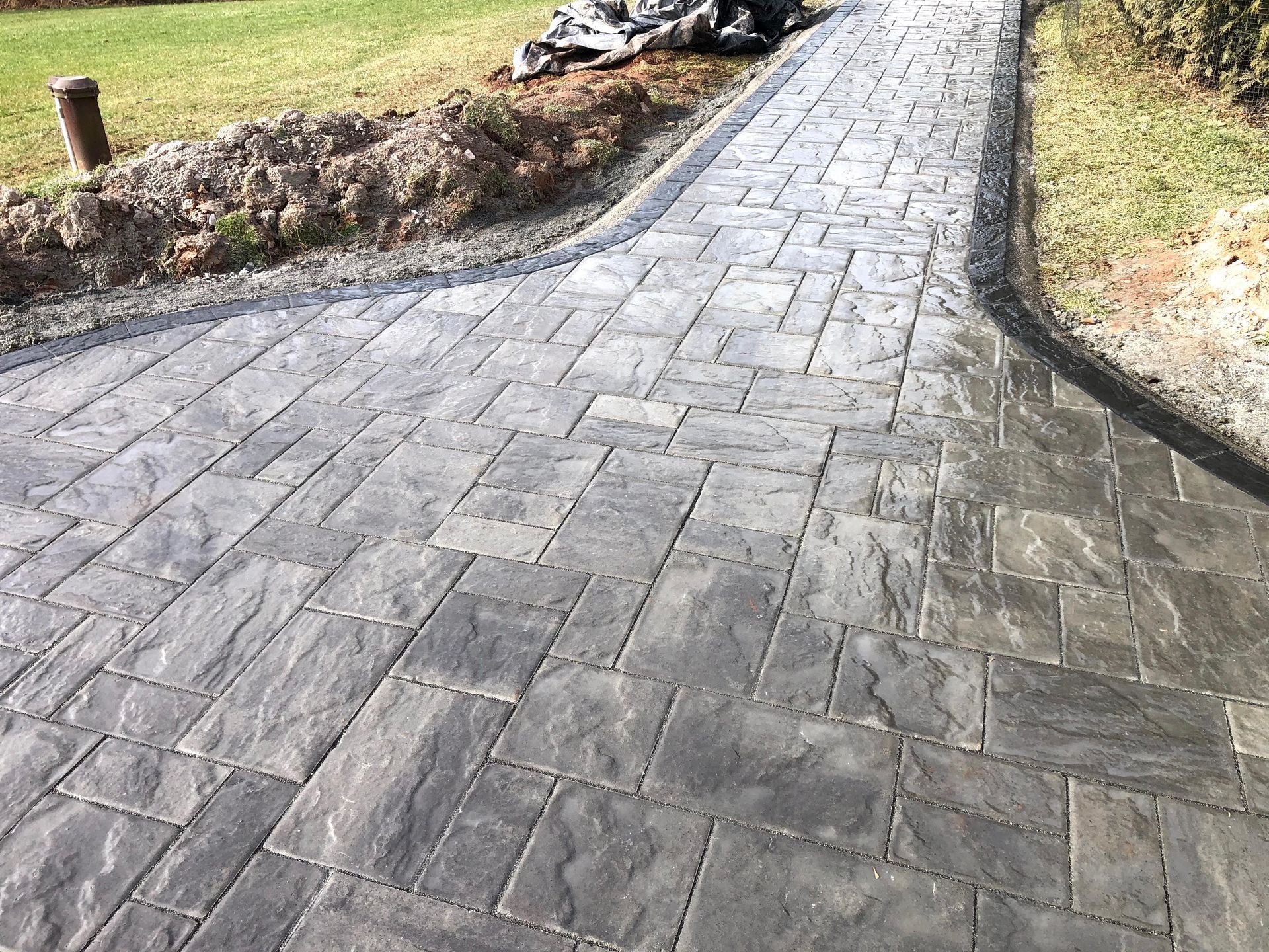 Curved gray stone pathway bordered by grass and dirt embankments outdoors