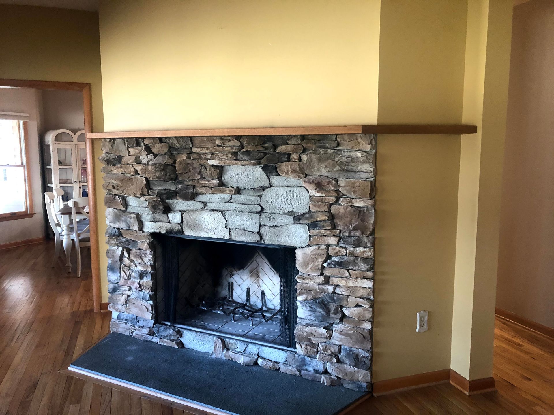 Stone fireplace in a yellow-walled room with dark hearth and wood trim