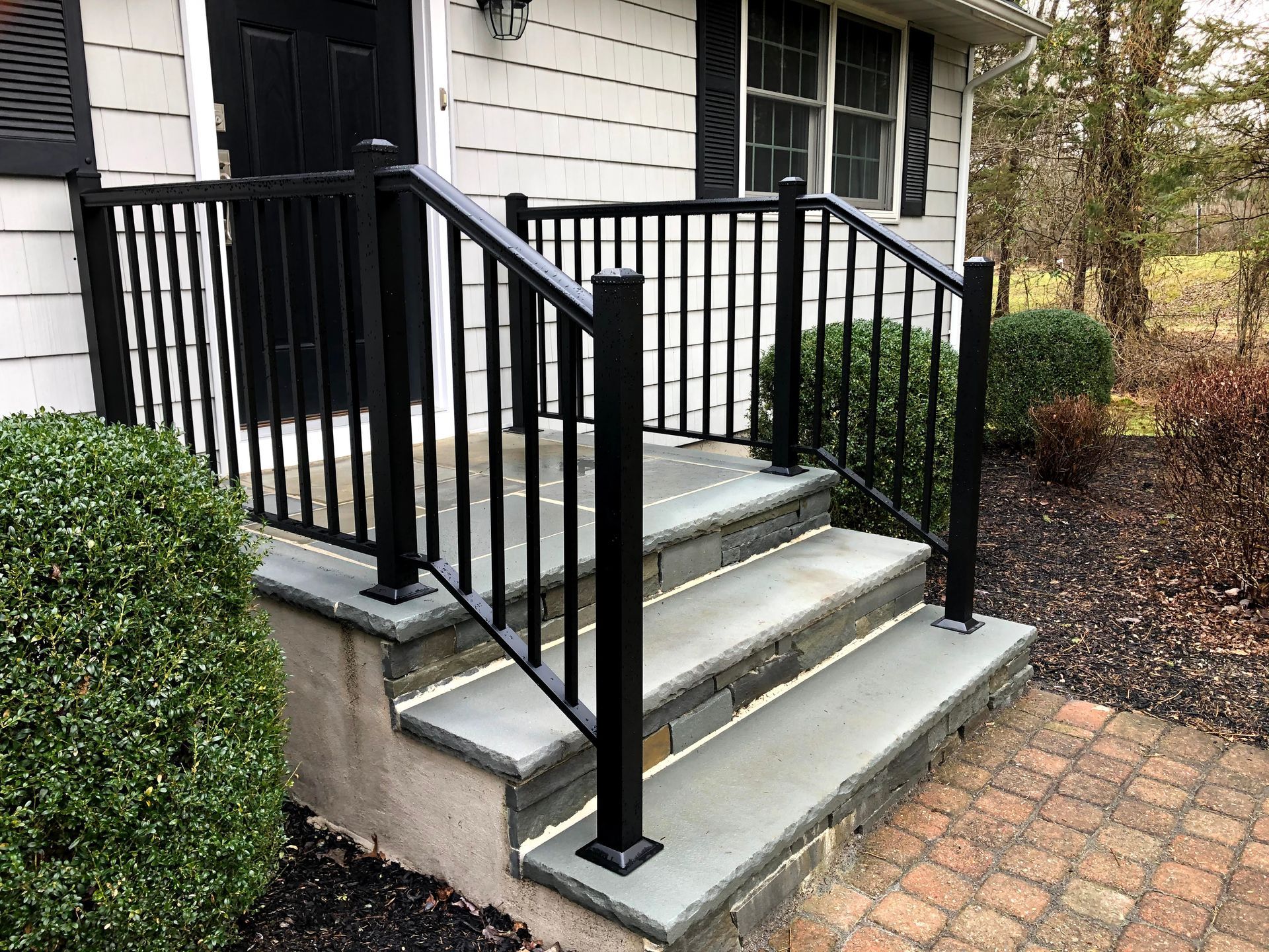 Front steps of a house with concrete stairs, black railings, and a brick walkway.