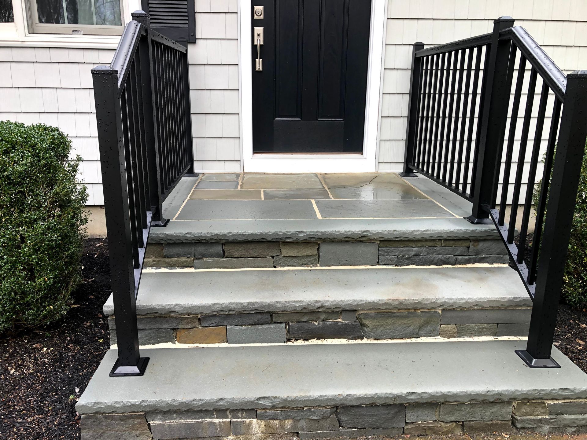 Front steps with black railings leading to a white house entrance door