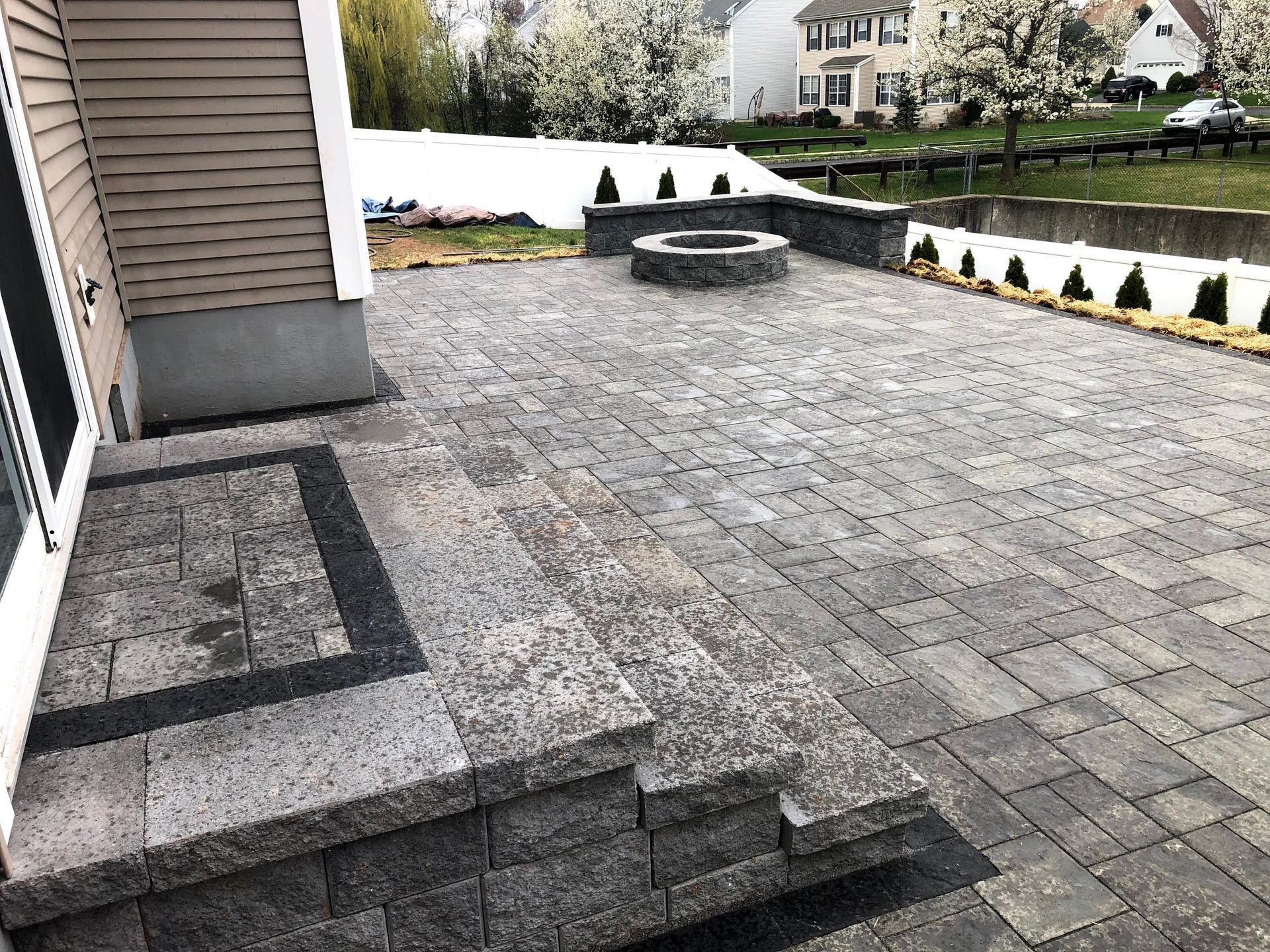 Patio with gray pavers, stone steps, and a circular fire pit in a suburban backyard