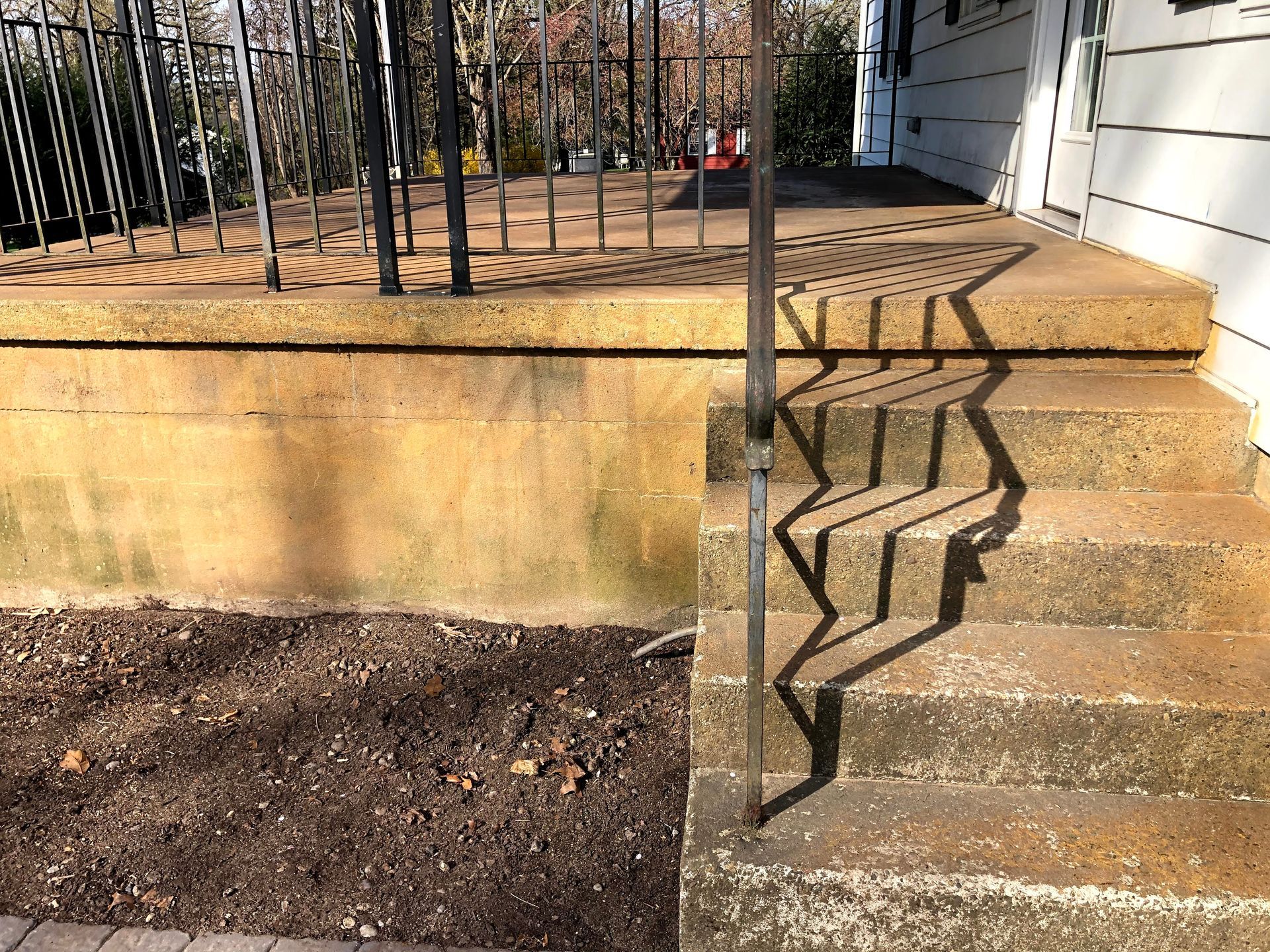 Outdoor concrete stairs with a black metal railing beside a raised planter wall