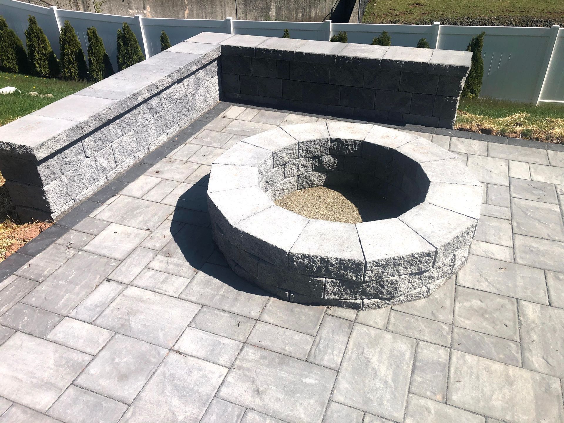 Stone circular fire pit with built-in bench seating on a paved patio in a landscaped yard