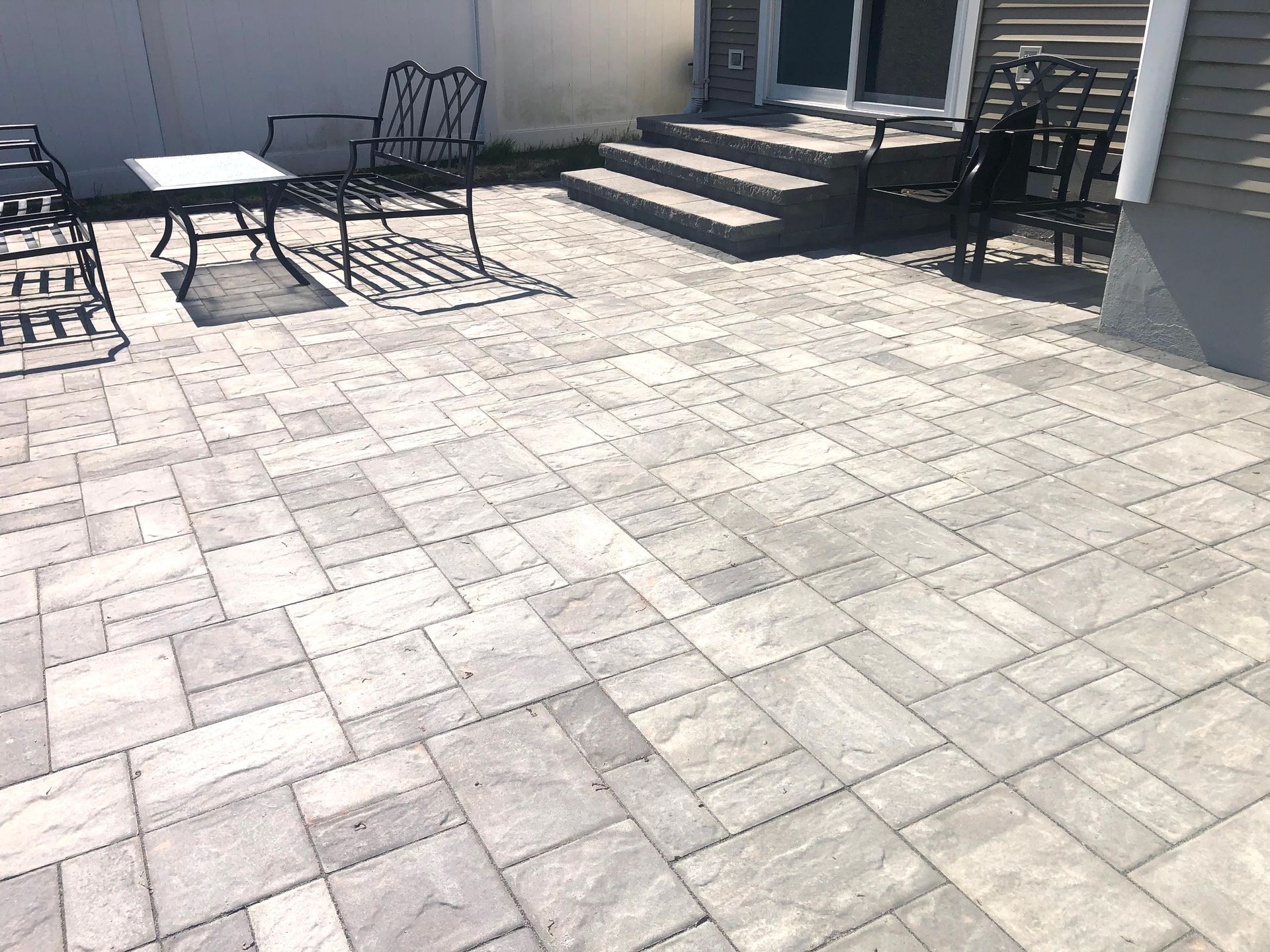 Patio with light stone pavers and black metal chairs near steps and a house wall