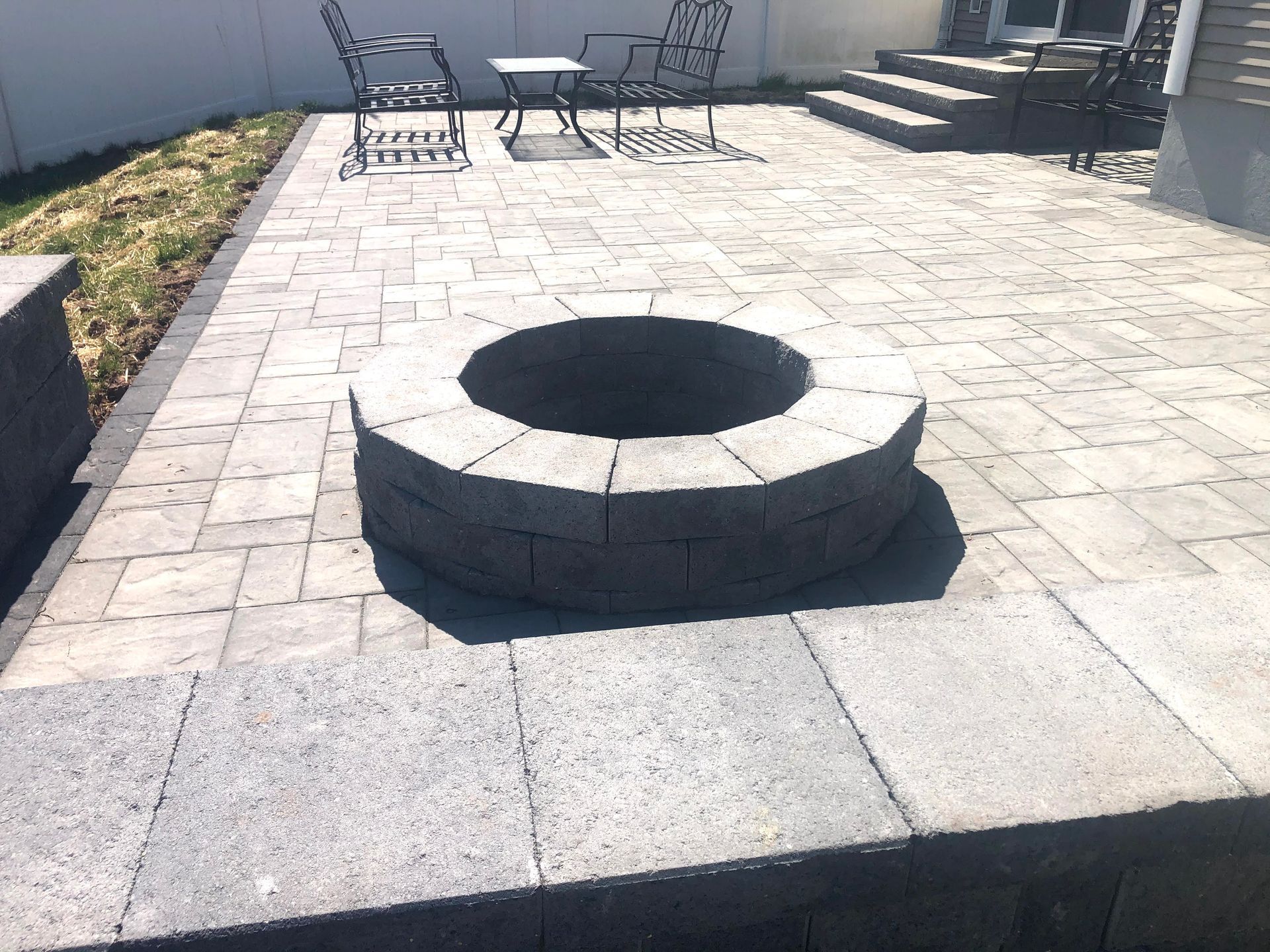 Stone patio with a circular fire pit and outdoor chairs in the background