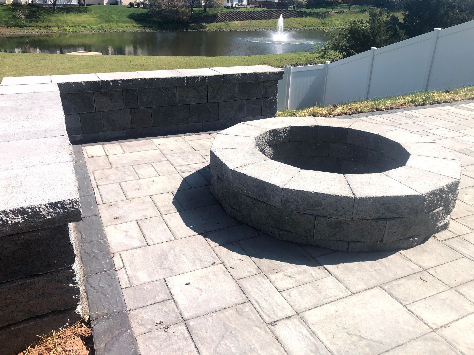 Stone fire pit on a paved patio beside a pond and fountain.