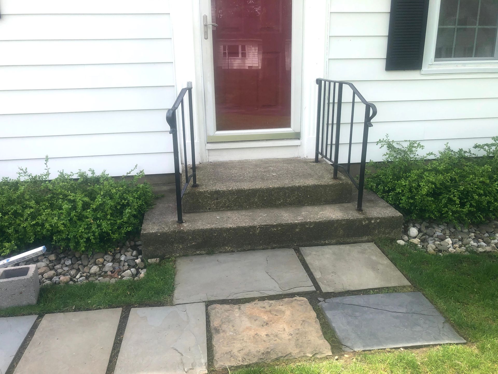 Front porch with red door, black railings, and stone walkway leading to a white house.