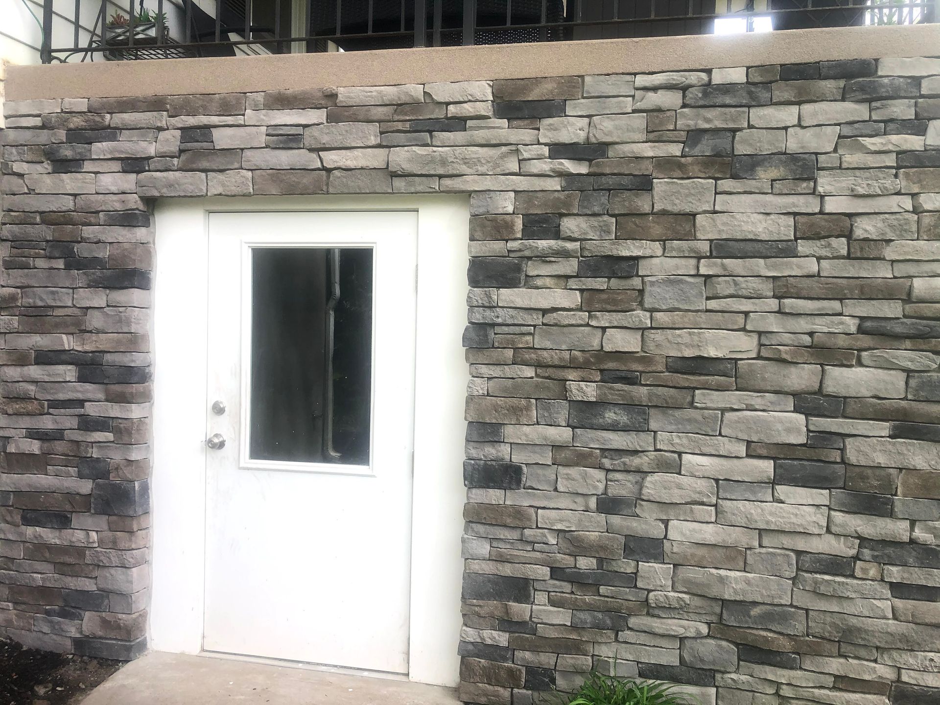 White door with a window set in a gray stone wall.