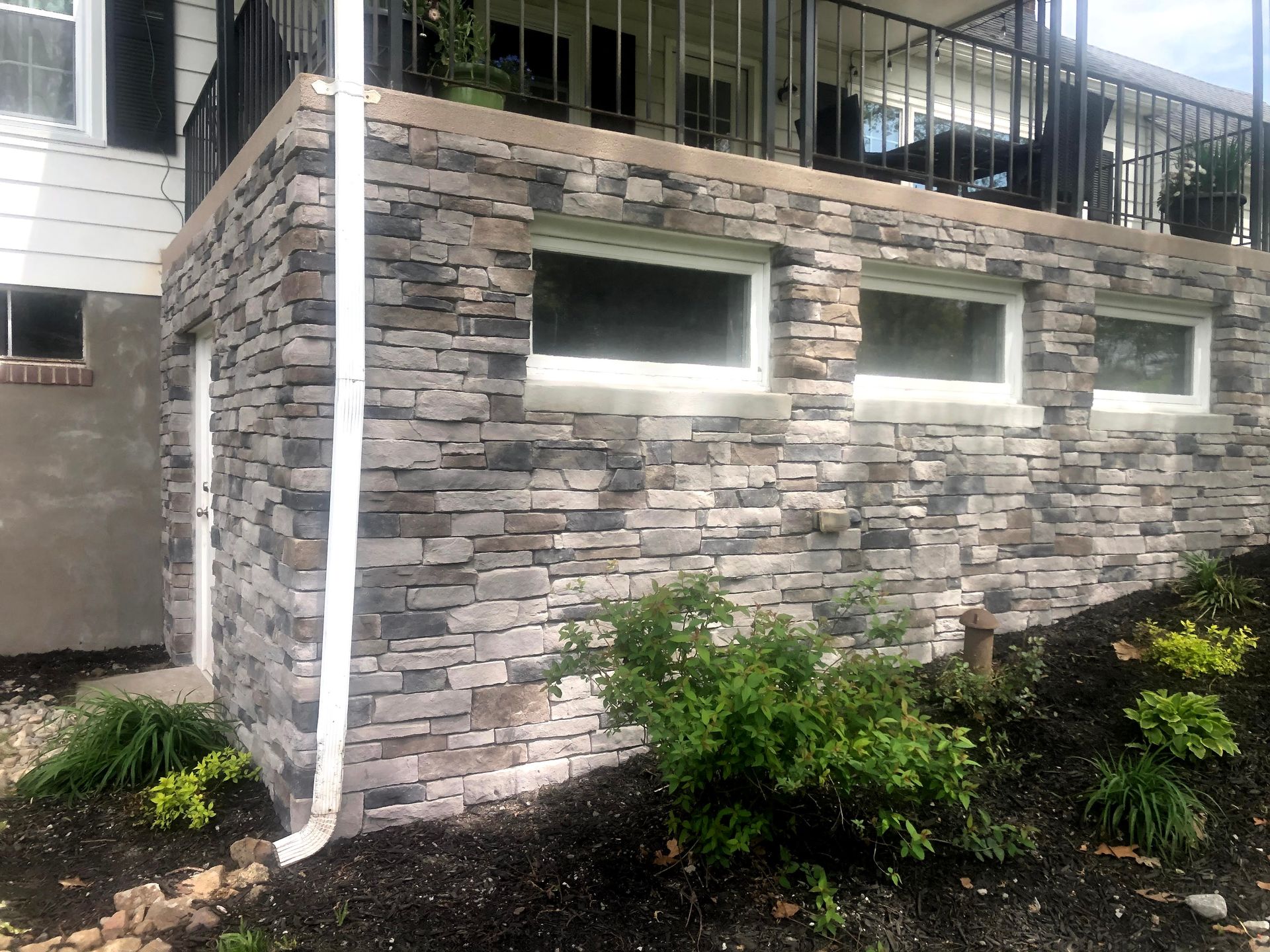 Stone exterior wall with small rectangular windows and shrubs along the base.