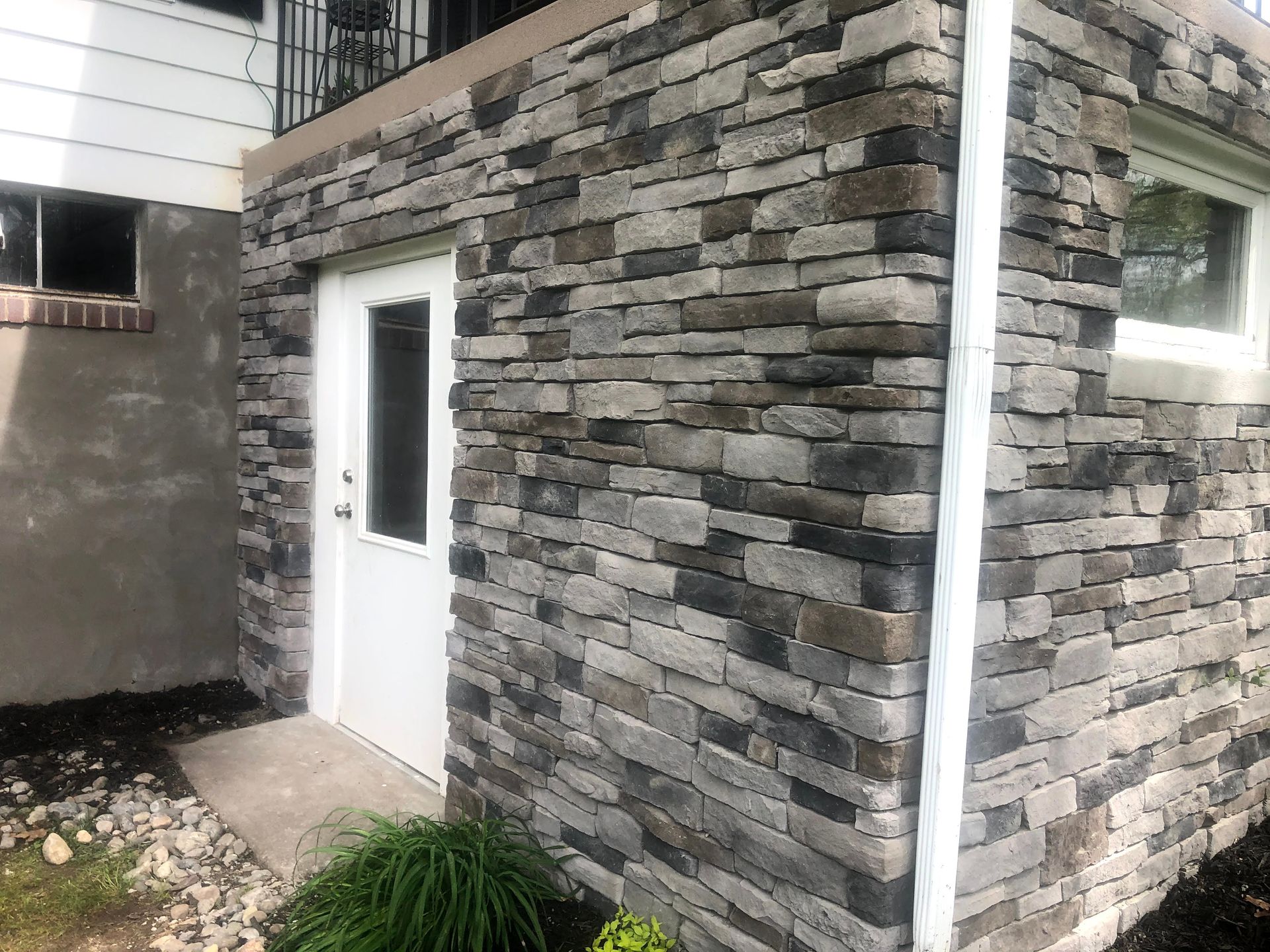 Gray stone building exterior with a white door and window beside a narrow walkway