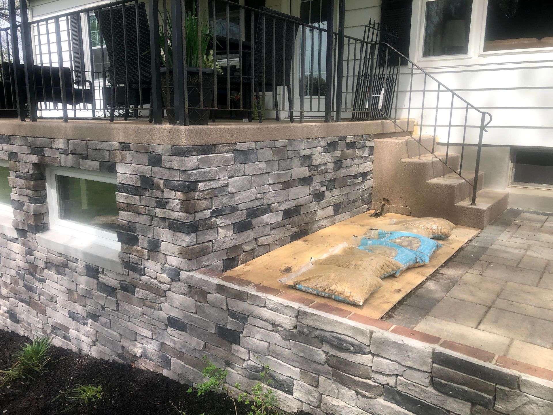 Stone patio and retaining wall beside a house, with steps and a covered object on the ground.